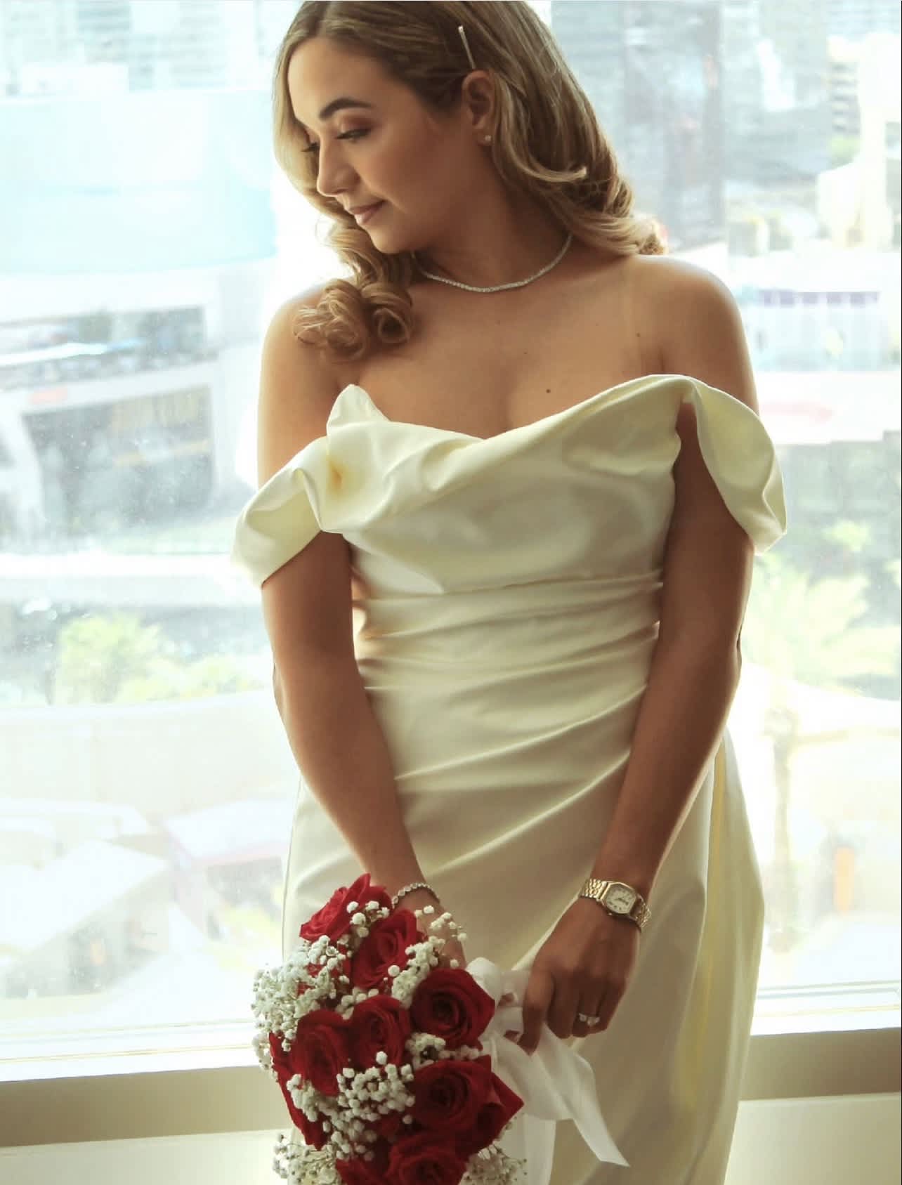Bride in an ivory off-shoulder gown holding a bouquet of red roses