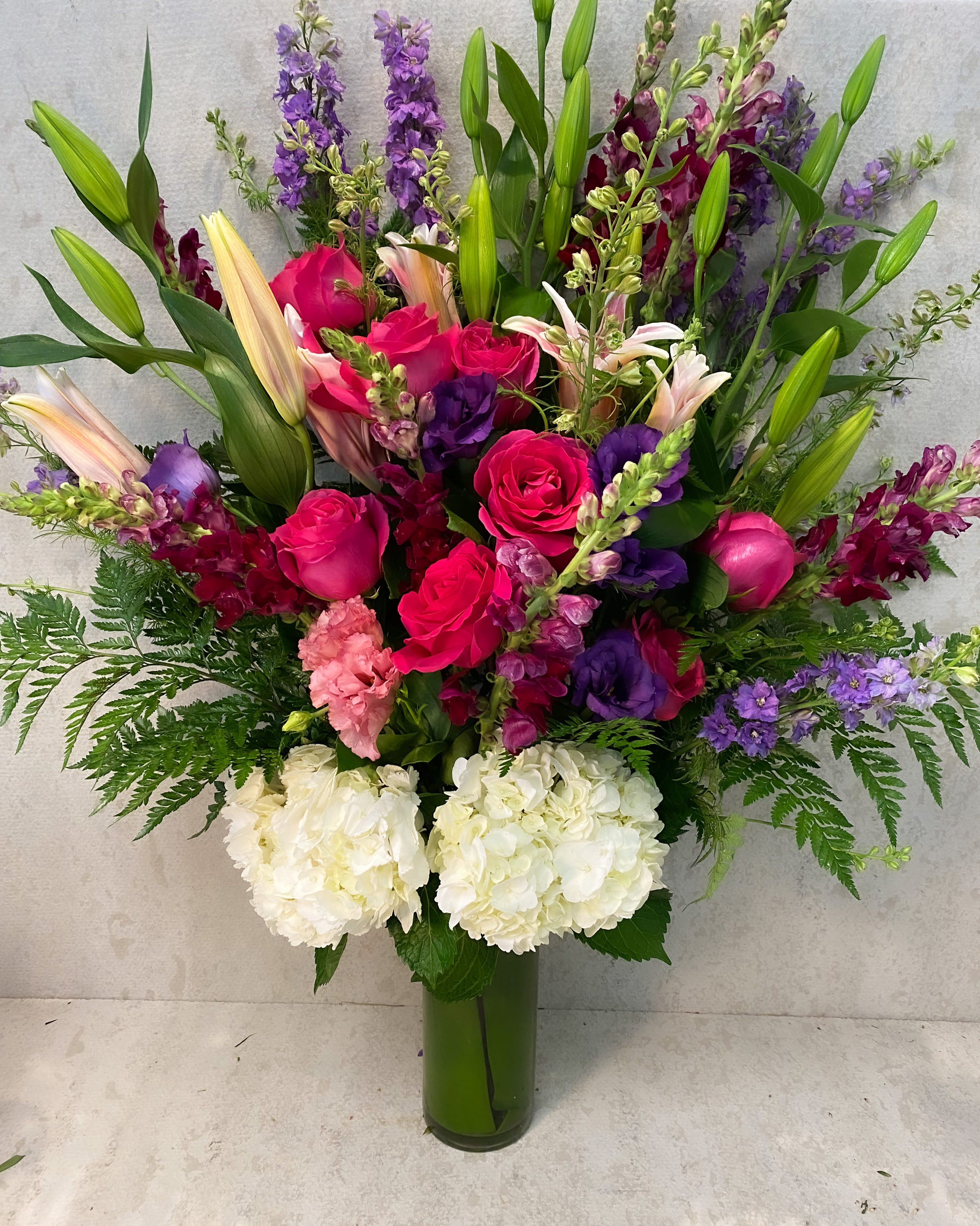 Tall bouquet of pink roses, lilies, and purple flowers in a glass vase