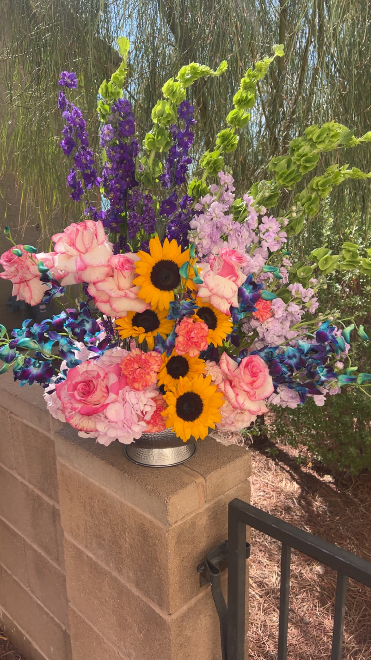 Colorful bouquet with sunflowers, pink roses, and purple blooms in a silver vase