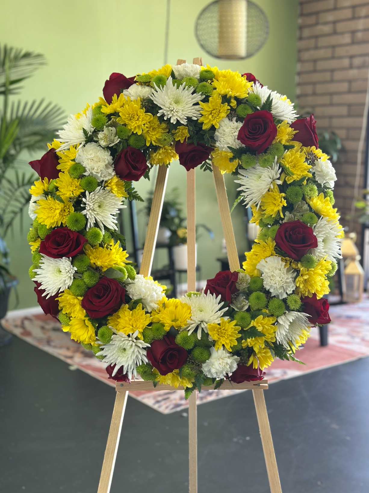 Circular floral wreath with red roses, white chrysanthemums, and yellow blooms on an easel