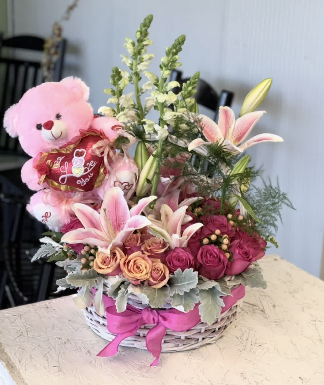 Pink teddy bear in a basket with pink lilies and roses