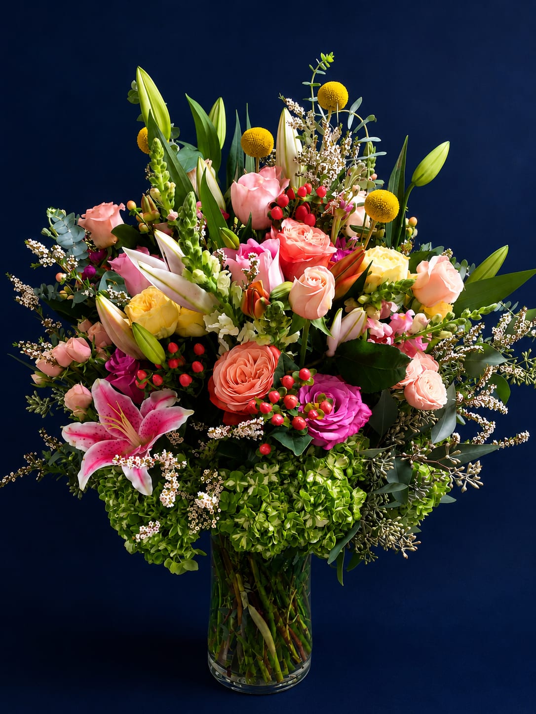 Midnight Garden Symphony - A luxurious garden-inspired arrangement designed to make a statement. Midnight Garden Symphony blends romantic pink lilies, blush and coral roses, vibrant fuchsia blooms, fresh green hydrangea, golden billy balls, and delicate seasonal accents with lush greenery and eucalyptus. Rich texture, bold color, and elegant movement create a bouquet that feels both modern and timeless — perfect for celebrations, heartfelt gifting, and sophisticated spaces.
