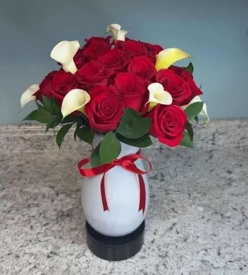 Bouquet of red roses and white calla lilies in a white vase with a red ribbon