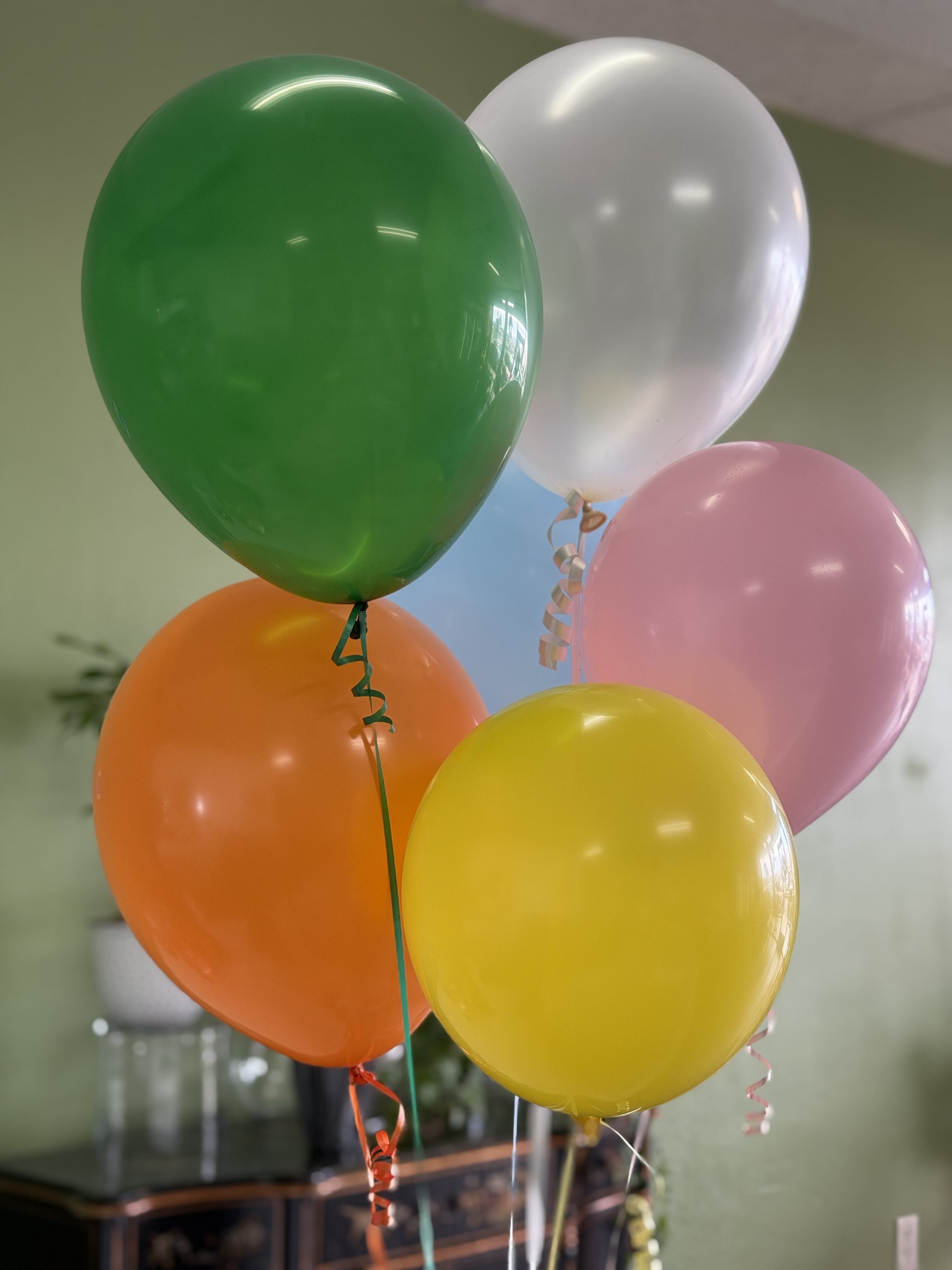 Cluster of colorful helium balloons in green, white, pink, orange, and yellow