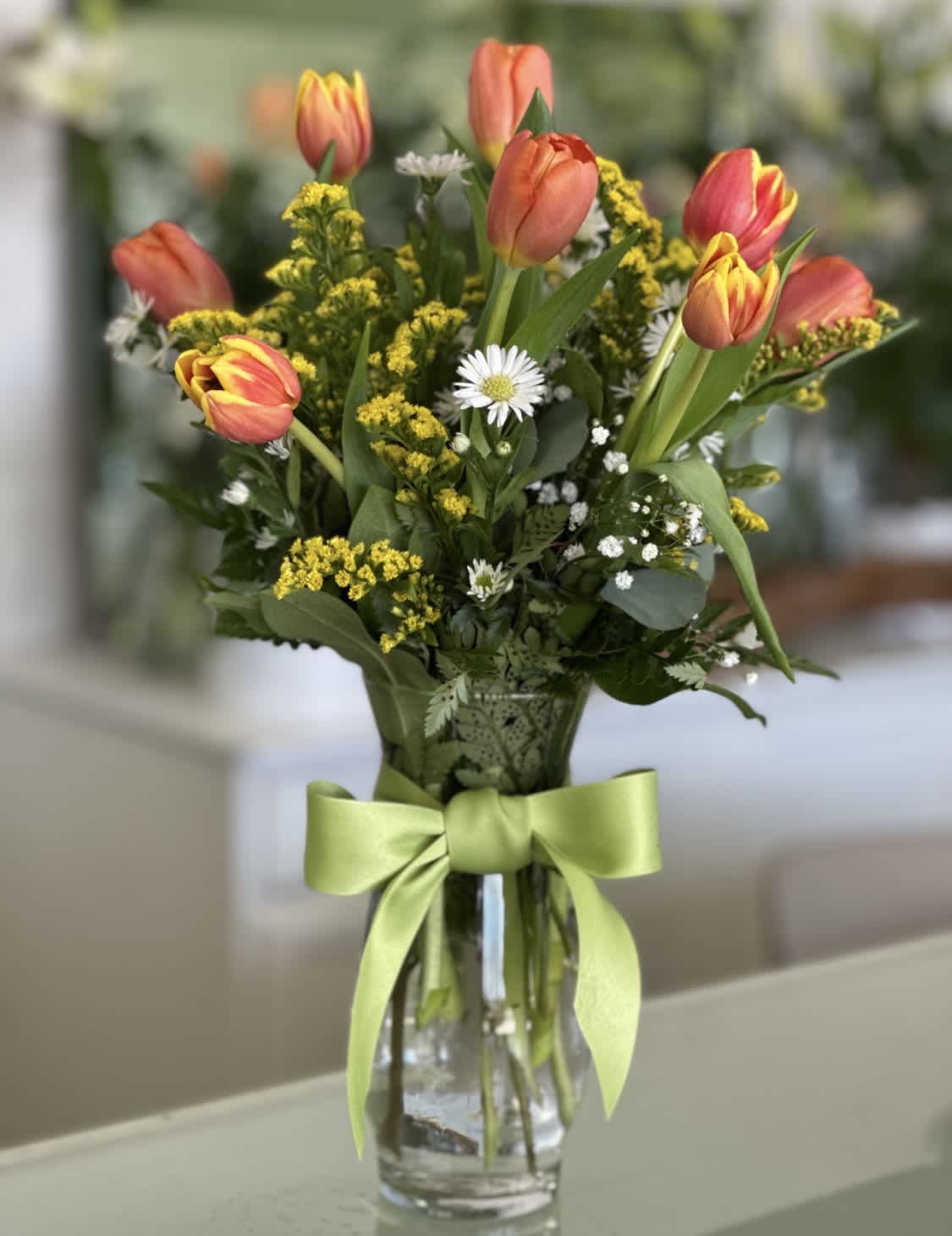 Bouquet of coral tulips and small white daisies in a glass vase with a green ribbon