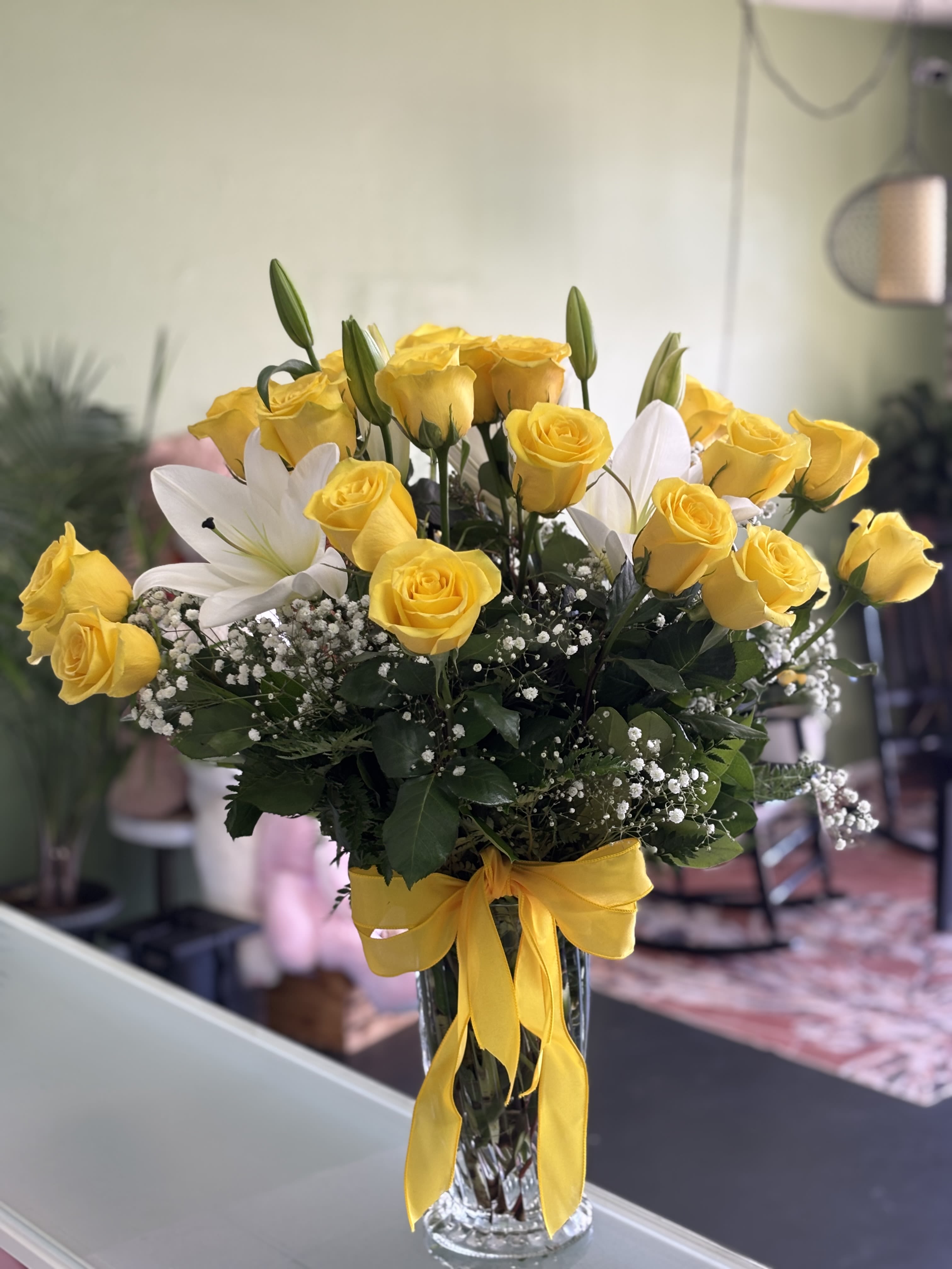 Yellow roses and white lilies in a clear glass vase with a yellow ribbon