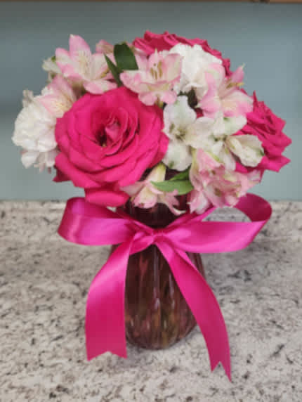 Pink and white flowers arranged in a glass vase with a pink ribbon