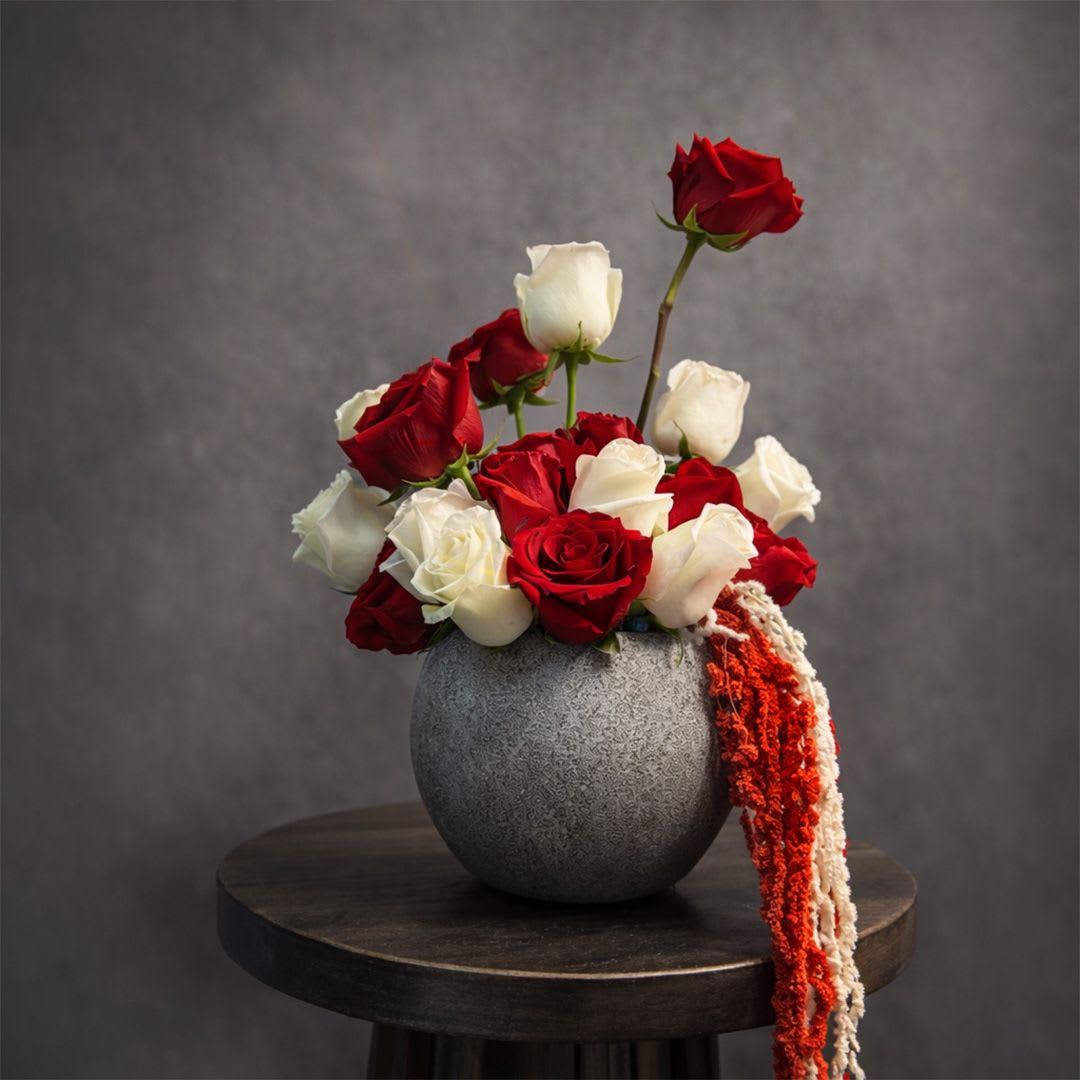 Crimson Balance - Crimson Balance is a striking arrangement of premium red and white roses designed in a modern bowl. The contrast between deep crimson and crisp ivory creates a bold yet harmonious composition that feels romantic, powerful, and timeless.  Structured with varying heights and a balanced silhouette, Crimson Balance is perfect for meaningful celebrations, romantic gestures, and elegant interior styling. A refined rose arrangement that blends passion with purity.