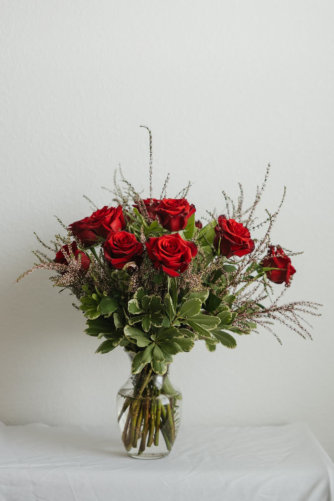 Red roses arranged in a clear glass vase with greenery