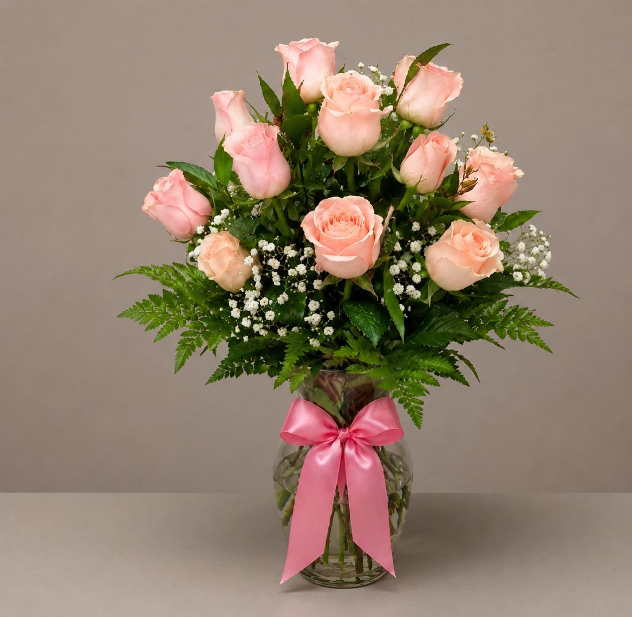 Pink roses in a glass vase with a pink ribbon