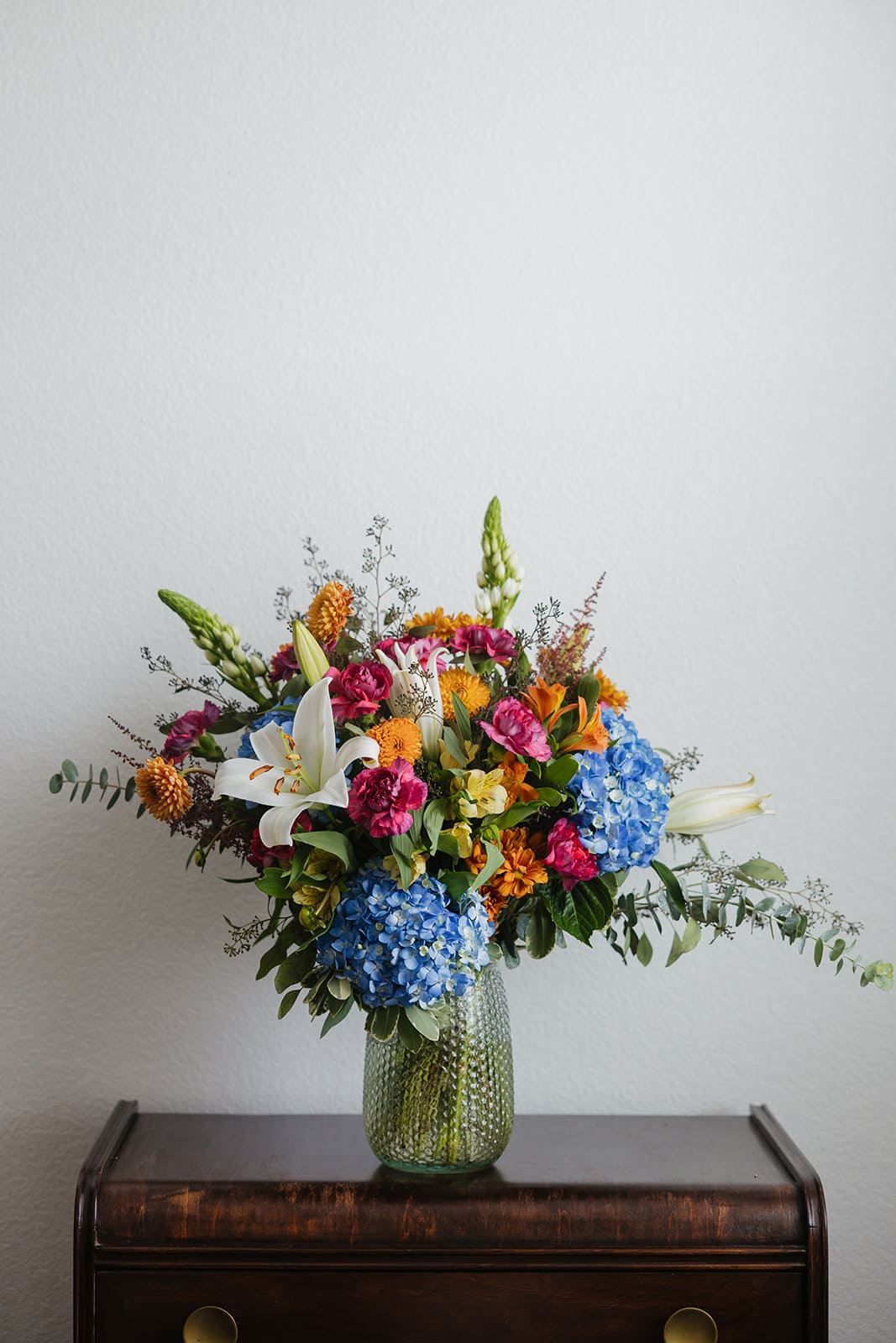 Colorful mixed bouquet in a green glass vase with lilies and hydrangeas