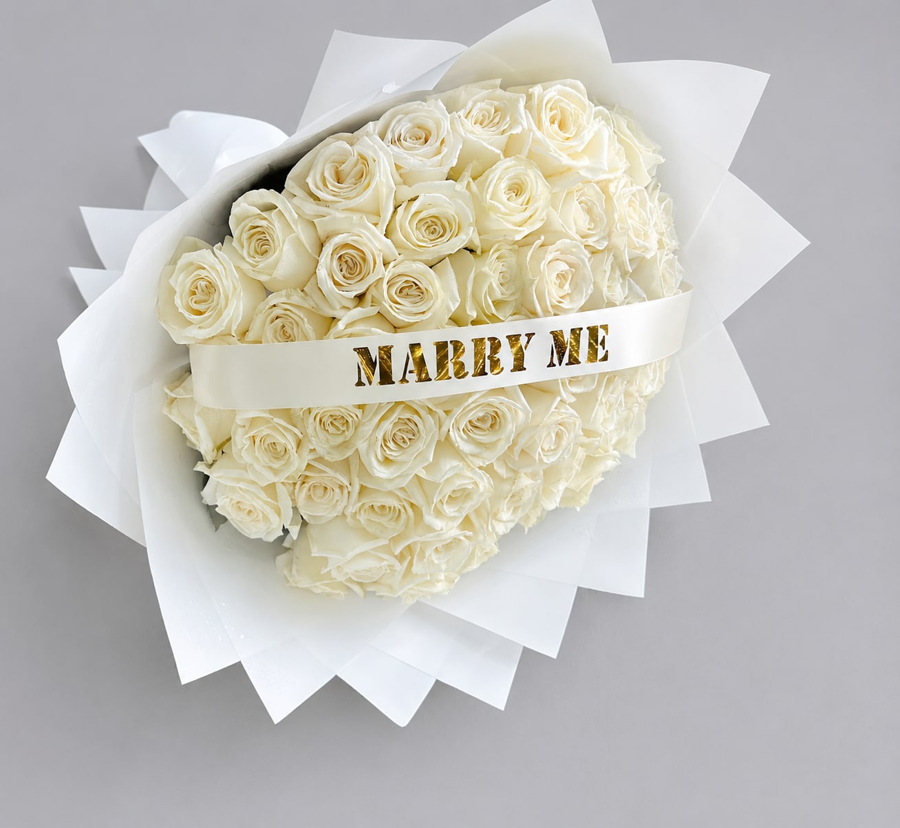 Bouquet of white roses wrapped with a "MARRY ME" ribbon