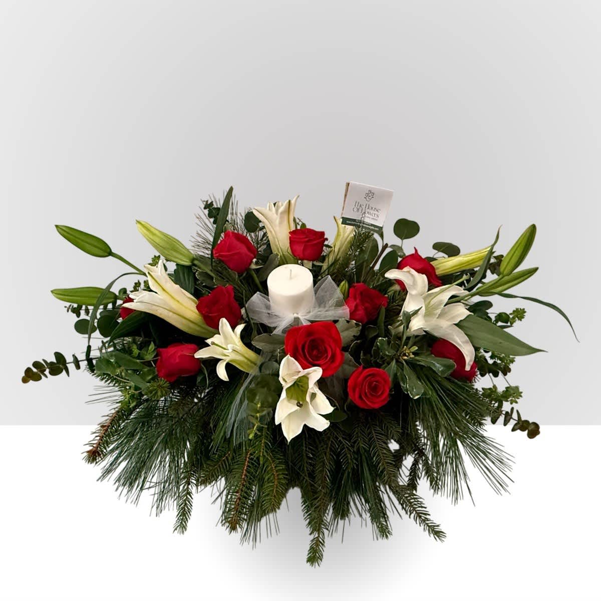 Red roses and white lilies arranged around a white candle in a low centerpiece