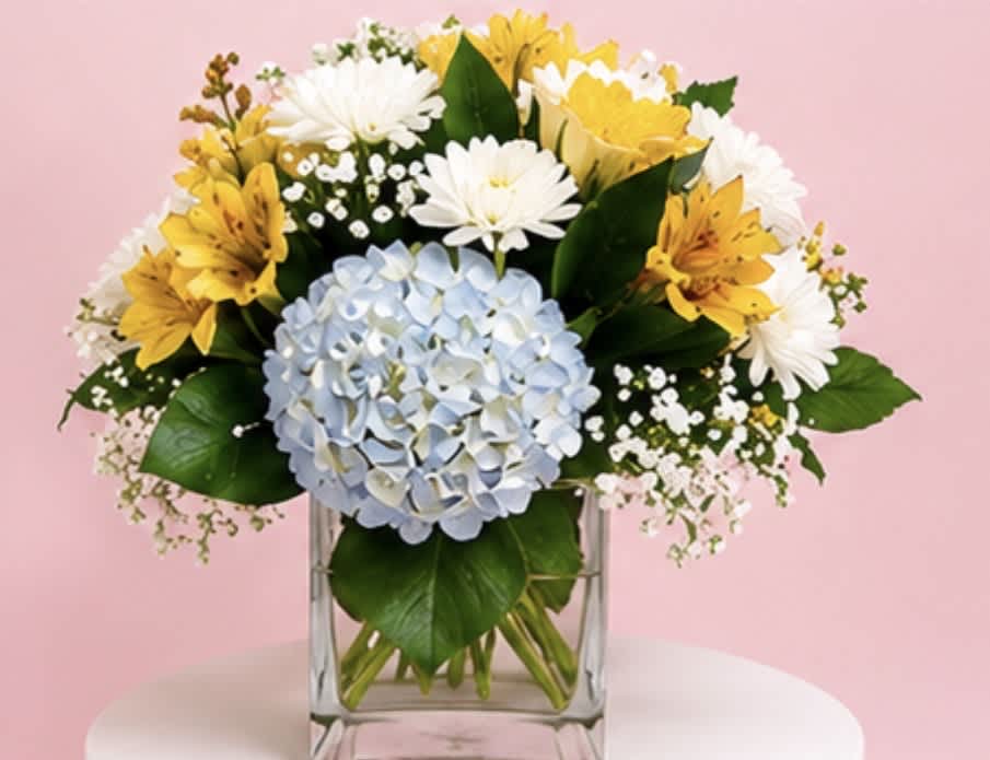 Bouquet of yellow and white flowers with a blue hydrangea in a clear glass vase
