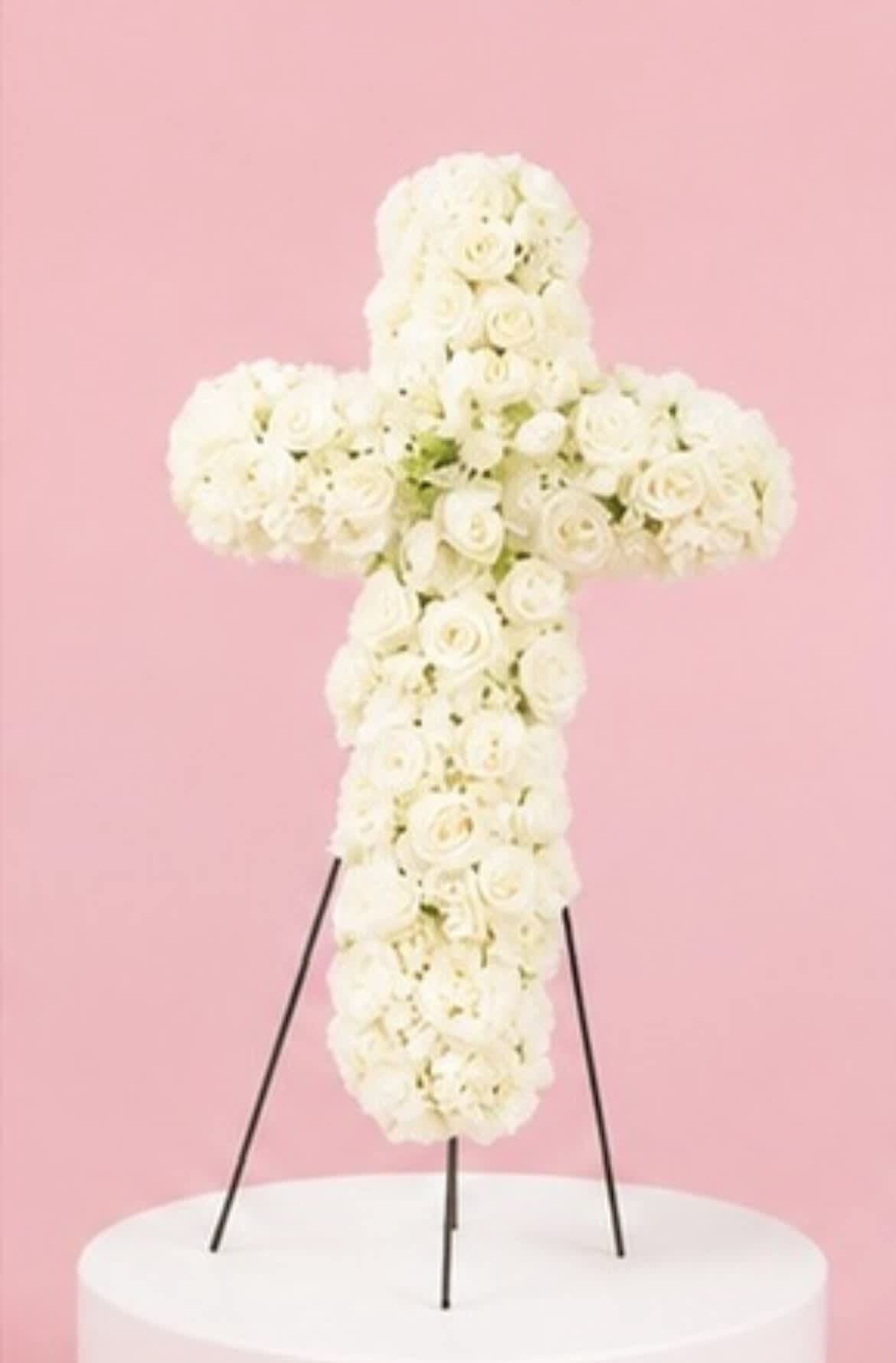 White rose cross-shaped floral arrangement on a stand against a pink background