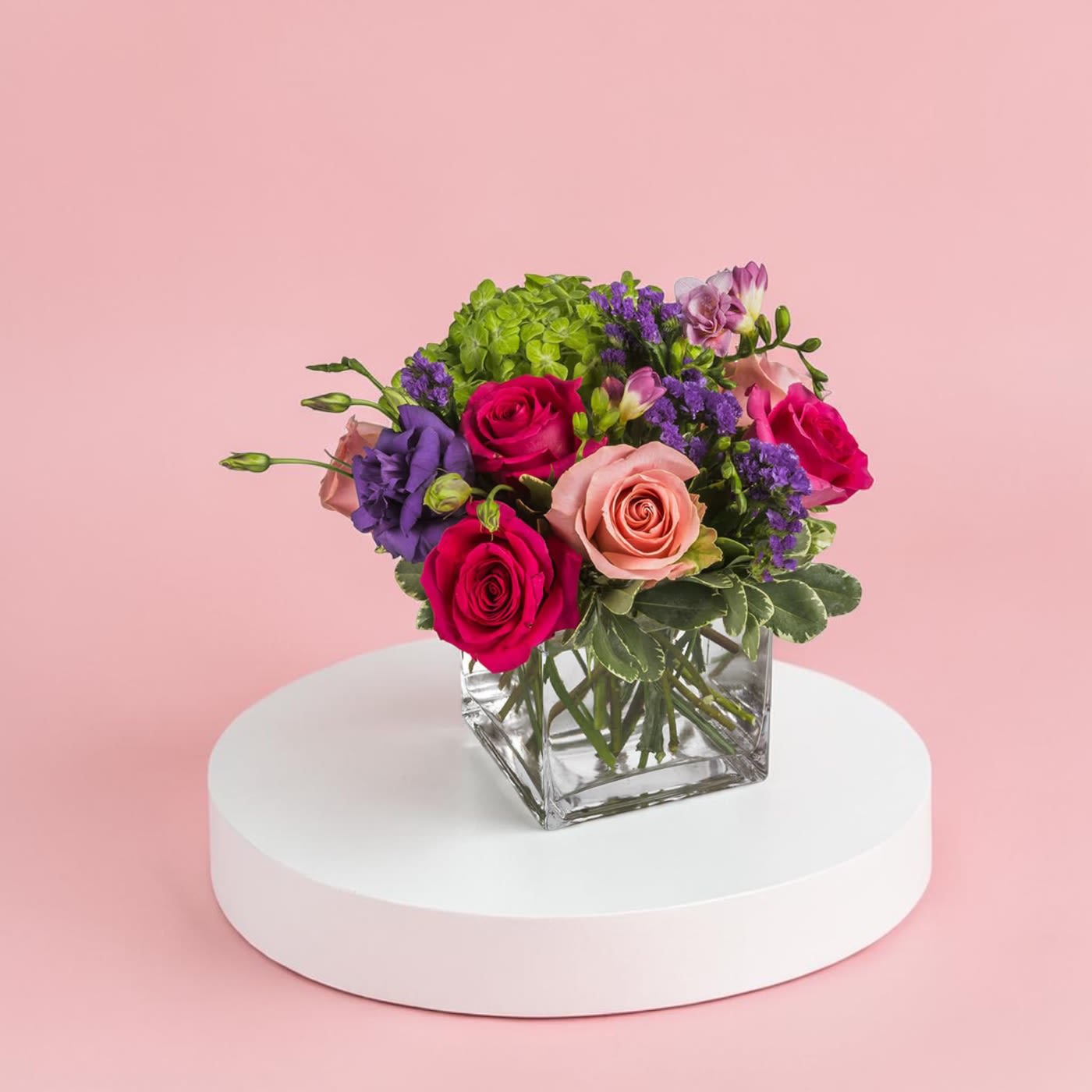 Spring Fling by BloomNation™ - This arrangement includes hot pink roses, pink roses, green hydrangea, freesia, lisianthus, purple statice. Spring Fling by BloomNation™ is a great gift for a birthday, get well, or just because.   APPROXIMATE DIMENSIONS: 12" H X 12" W