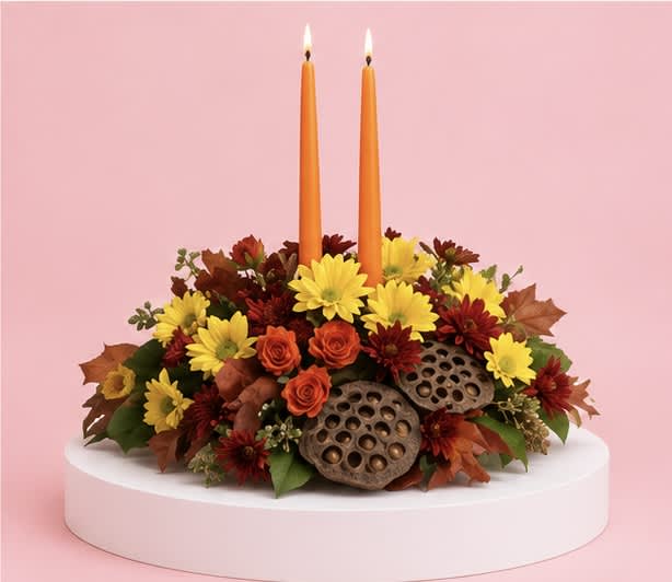 Autumn floral centerpiece with two orange taper candles on a white pedestal