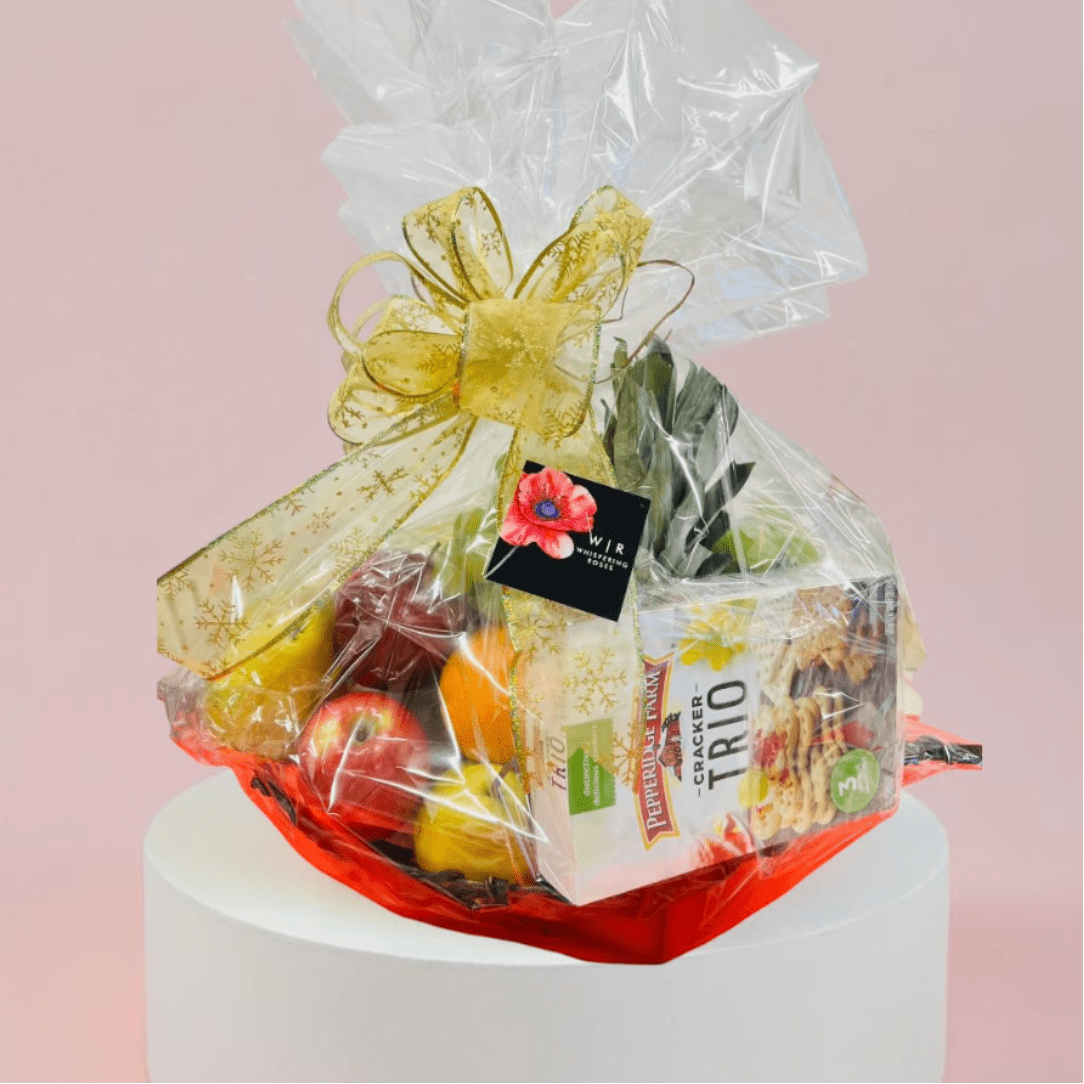 Gift basket with snacks and fruit wrapped in clear cellophane and a gold bow