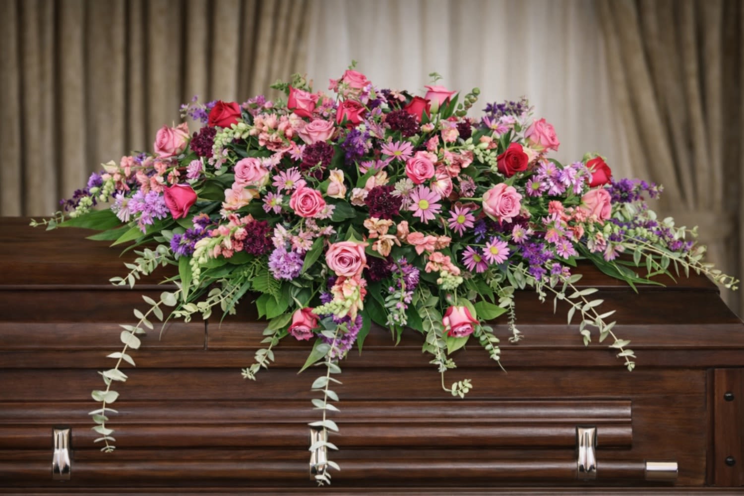Divine Casket Spray  - The Divine Casket Spray from FloralFabulous is a vibrant and expressive tribute designed to celebrate a life filled with beauty, personality, and cherished memories. This lush arrangement features a stunning mix of pink roses, purple blooms, and seasonal flowers, artfully arranged with flowing greenery for a soft cascading effect.  The blend of pink and purple tones symbolizes love, admiration, grace, and remembrance, making this arrangement a meaningful choice for honoring a loved one with a unique and uplifting tribute. Designed to rest gracefully atop the casket, this spray creates a striking and comforting focal point during funeral and memorial services.