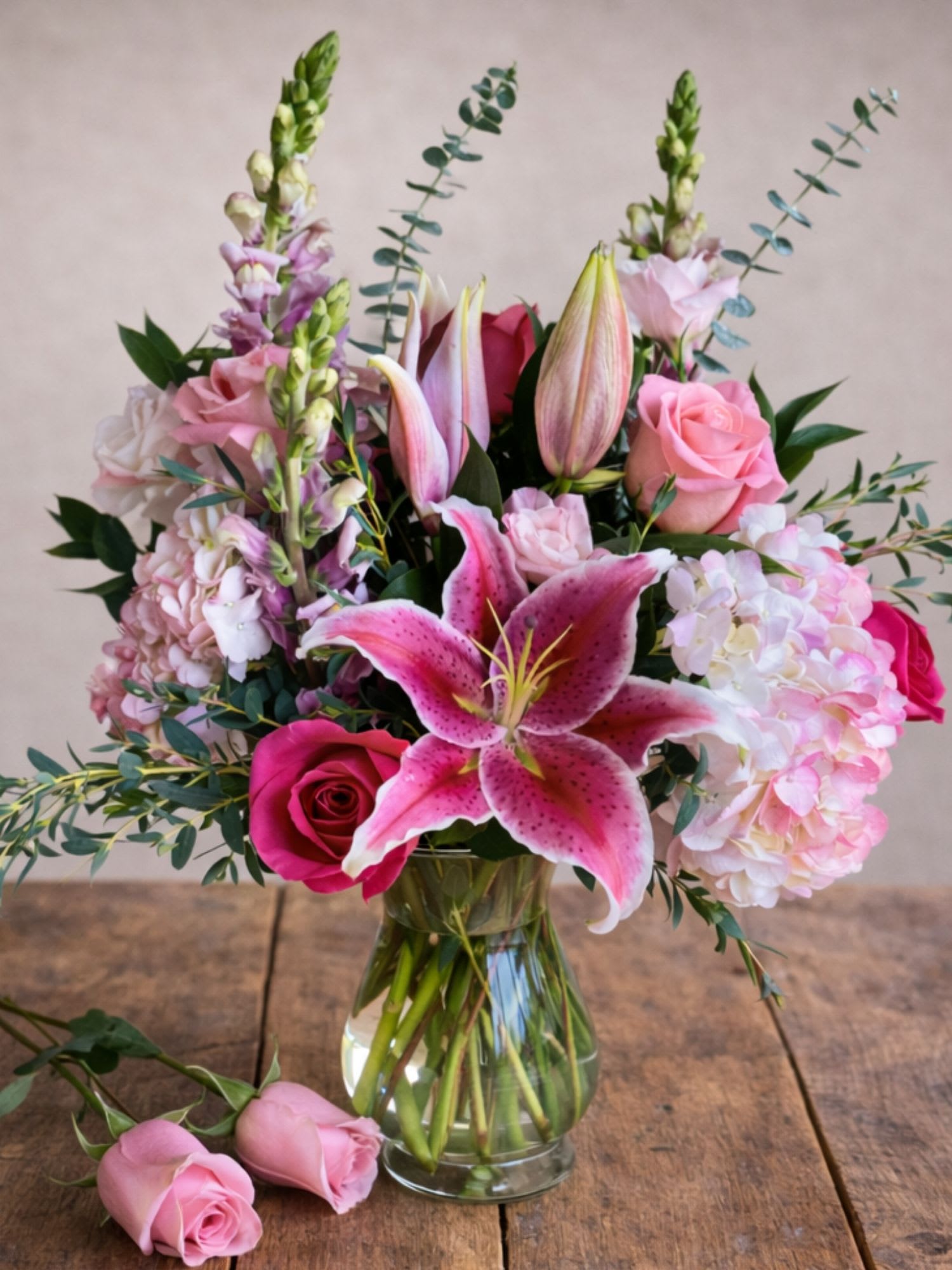 Pink lilies and roses arranged in a clear glass vase