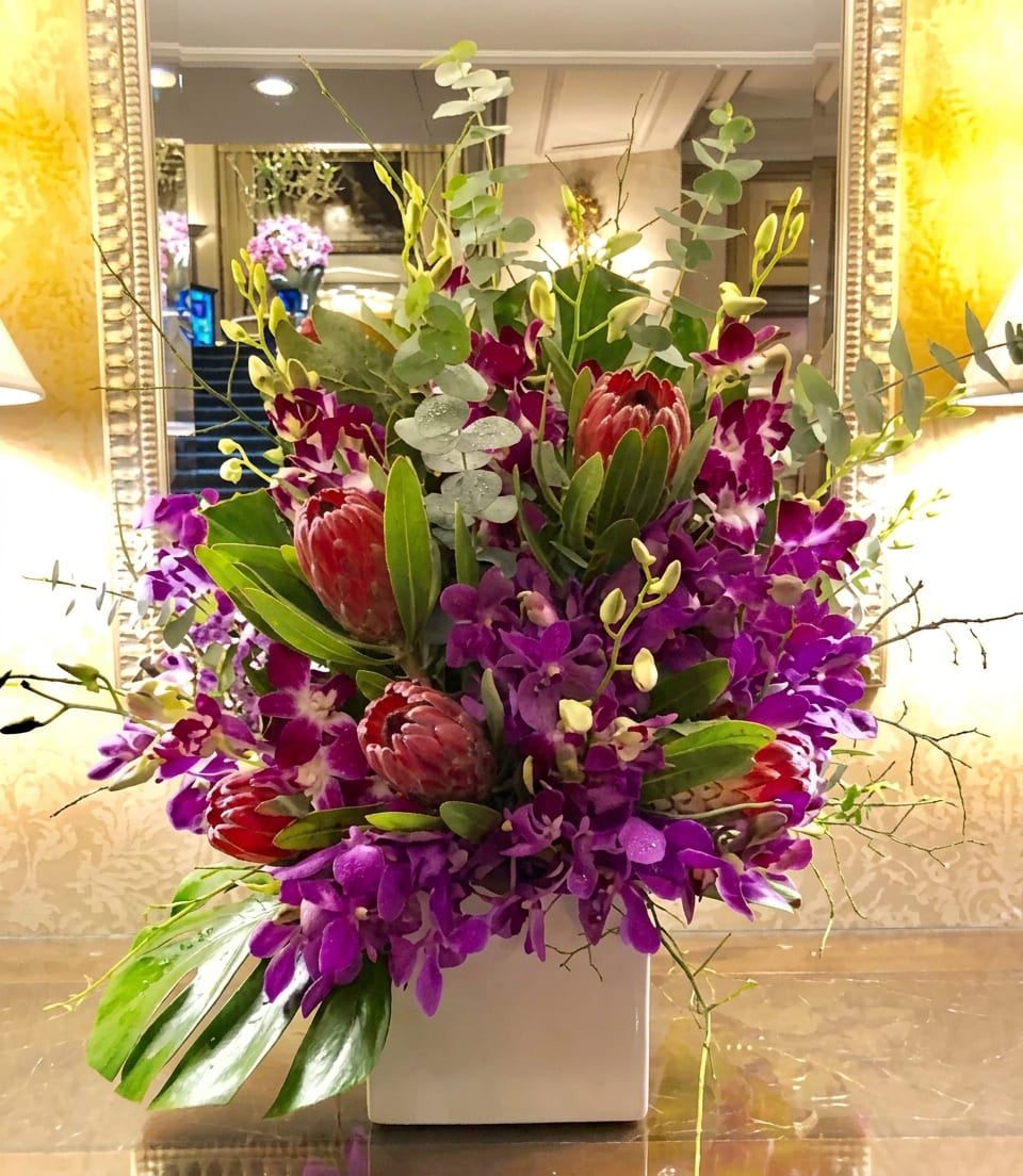 Purple orchids and red protea in a white square vase