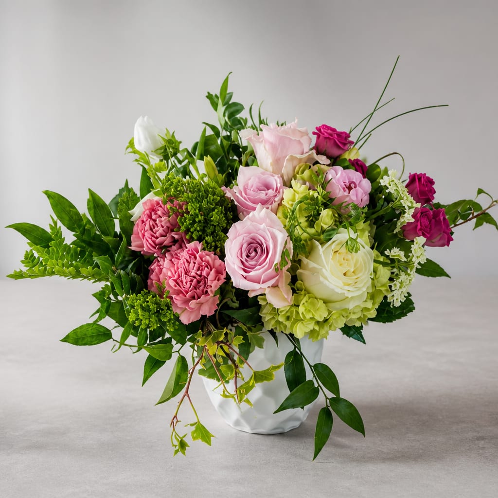 Mixed pink, white, and green floral arrangement in a white vase
