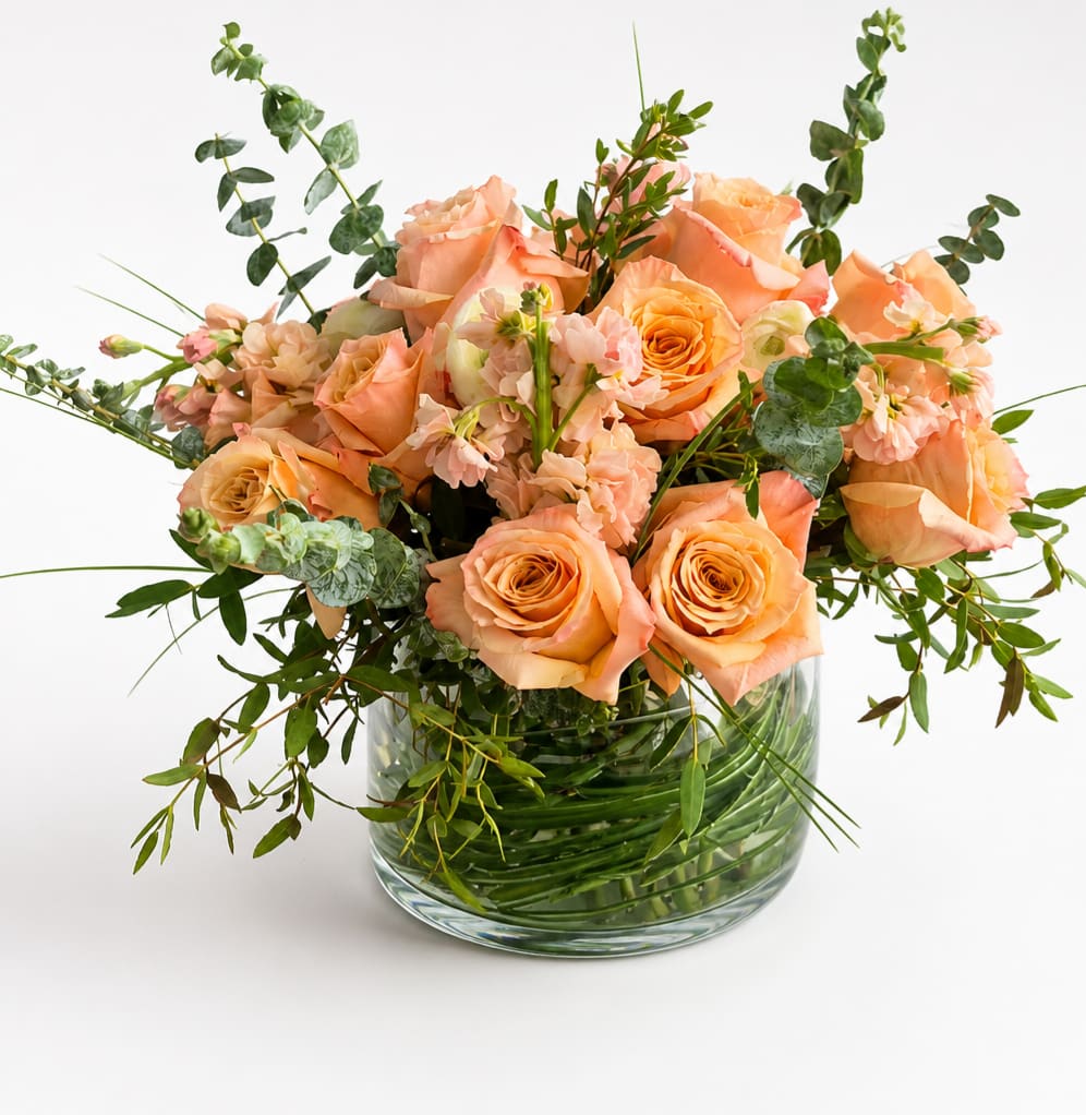 Peach roses and small pink flowers in a clear glass vase