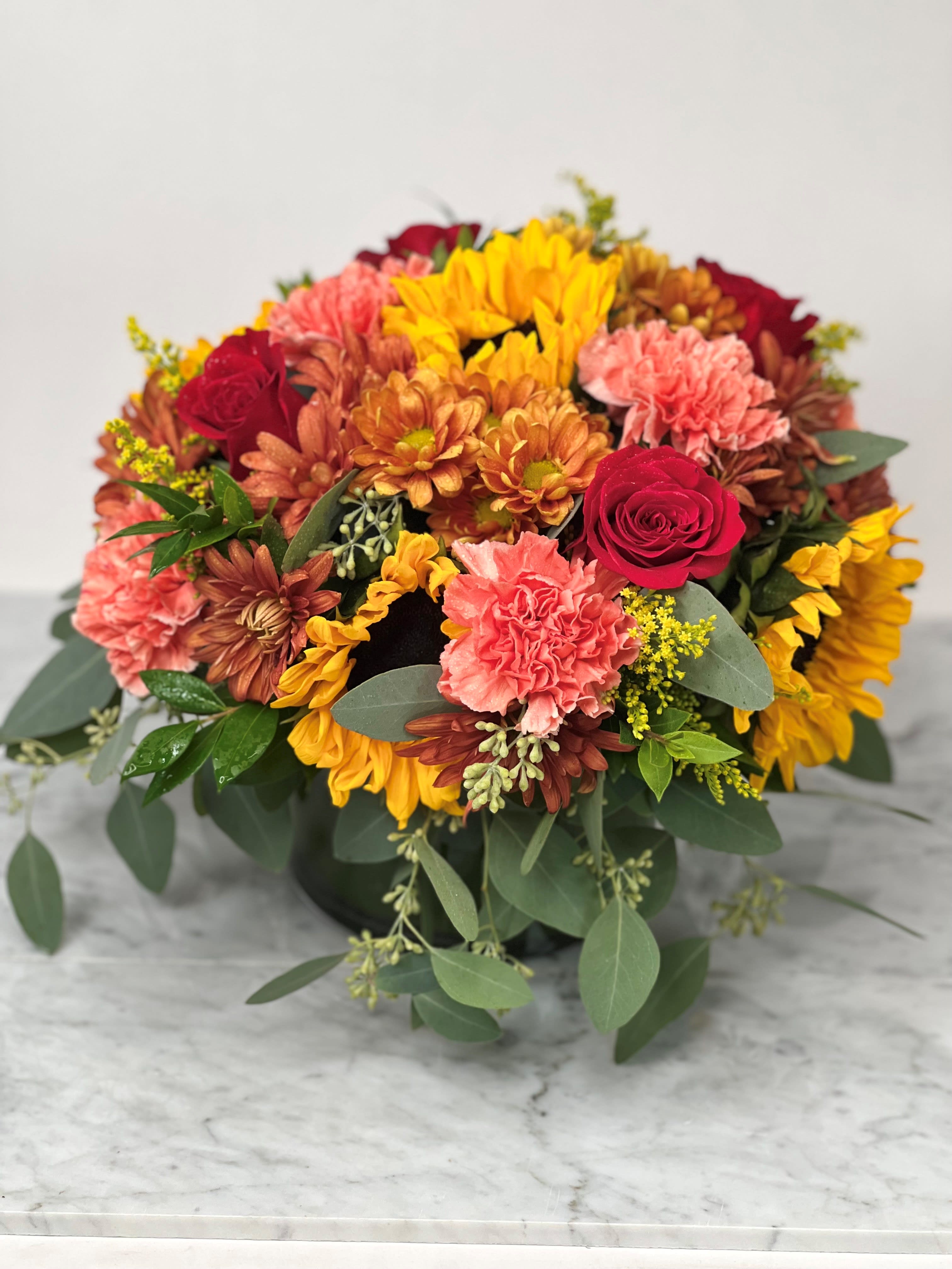 Mixed bouquet of sunflowers, roses, and carnations in a low container