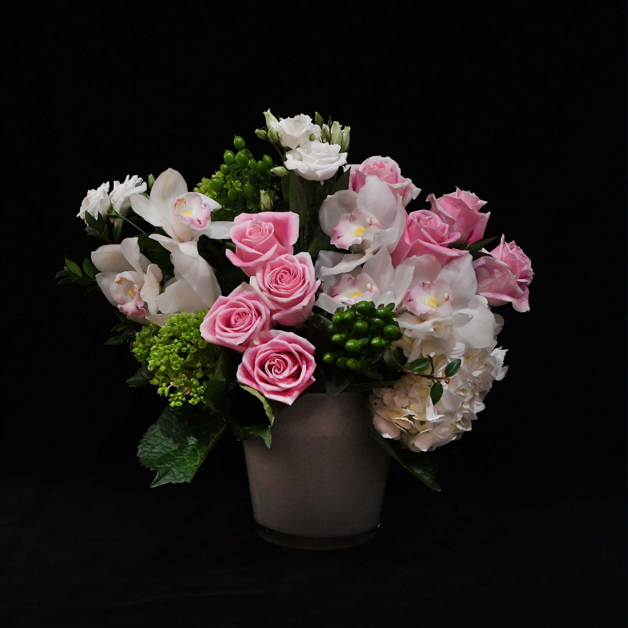 Peaceful Arrangement - Beautiful pink roses and white orchids arranged atop a bed of green and white hydrangea.  Designed in a chic, white glass vase.