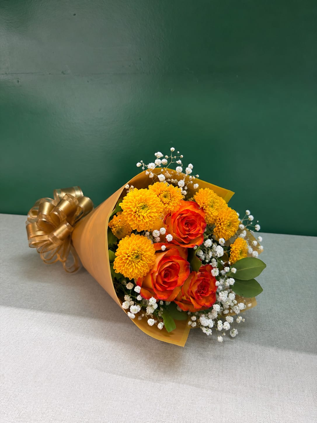 Bouquet of orange roses and yellow chrysanthemums wrapped in gold paper