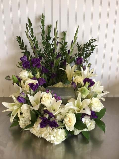 White lilies and purple flowers arranged around a rectangular container