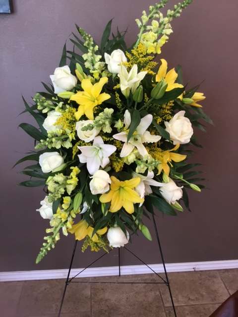 Standing floral spray with white roses and yellow lilies on a metal easel