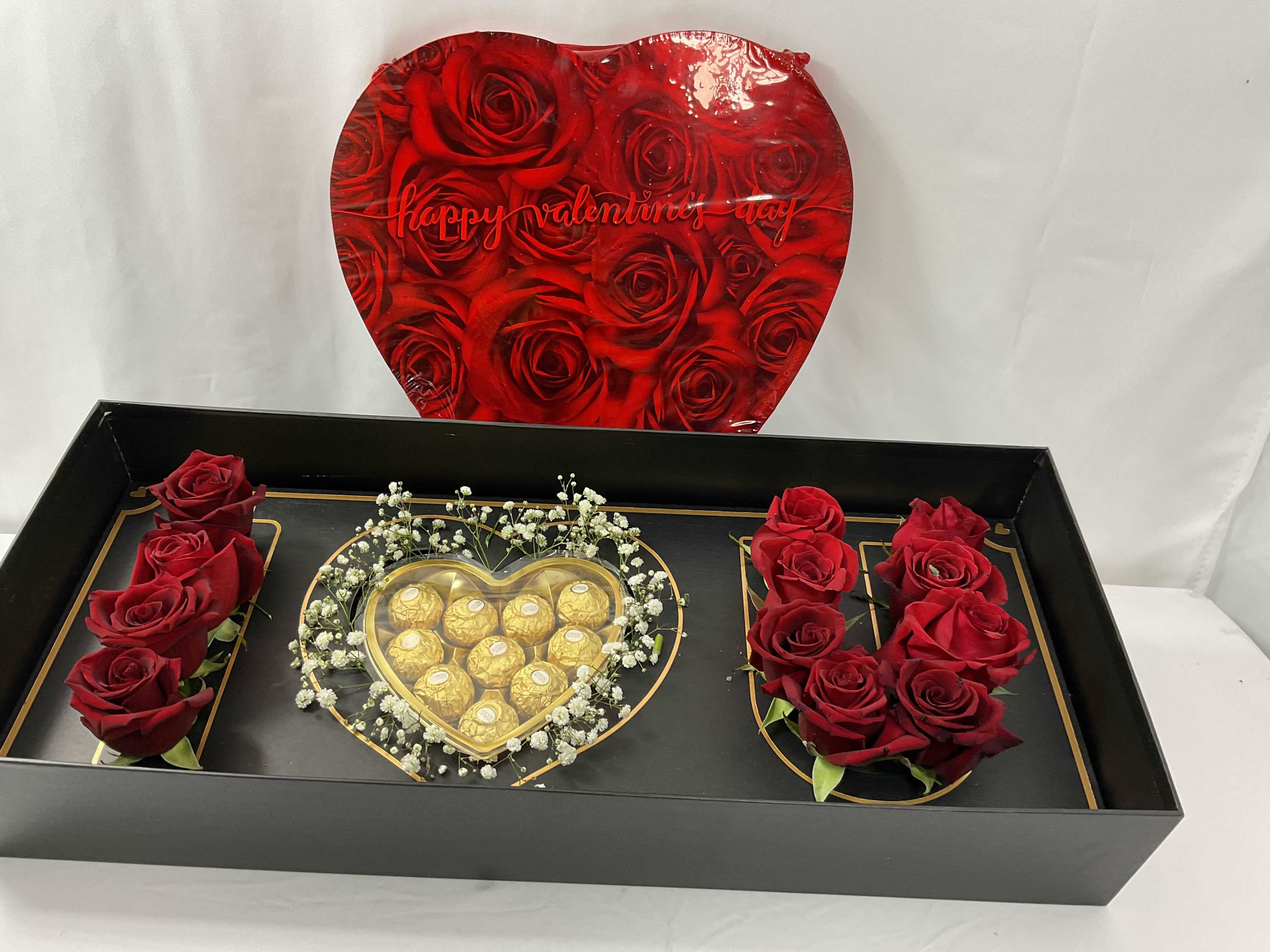 Red roses and chocolates arranged in a black gift box with a heart lid