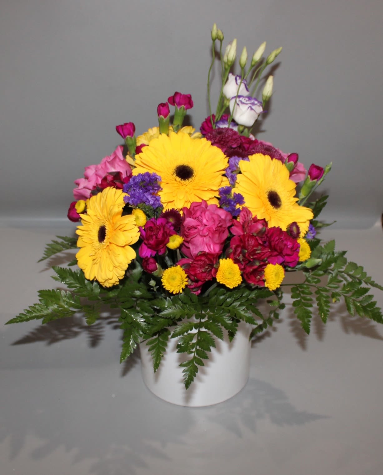 Bright mixed flower arrangement in a white pot with yellow daisies and pink blooms