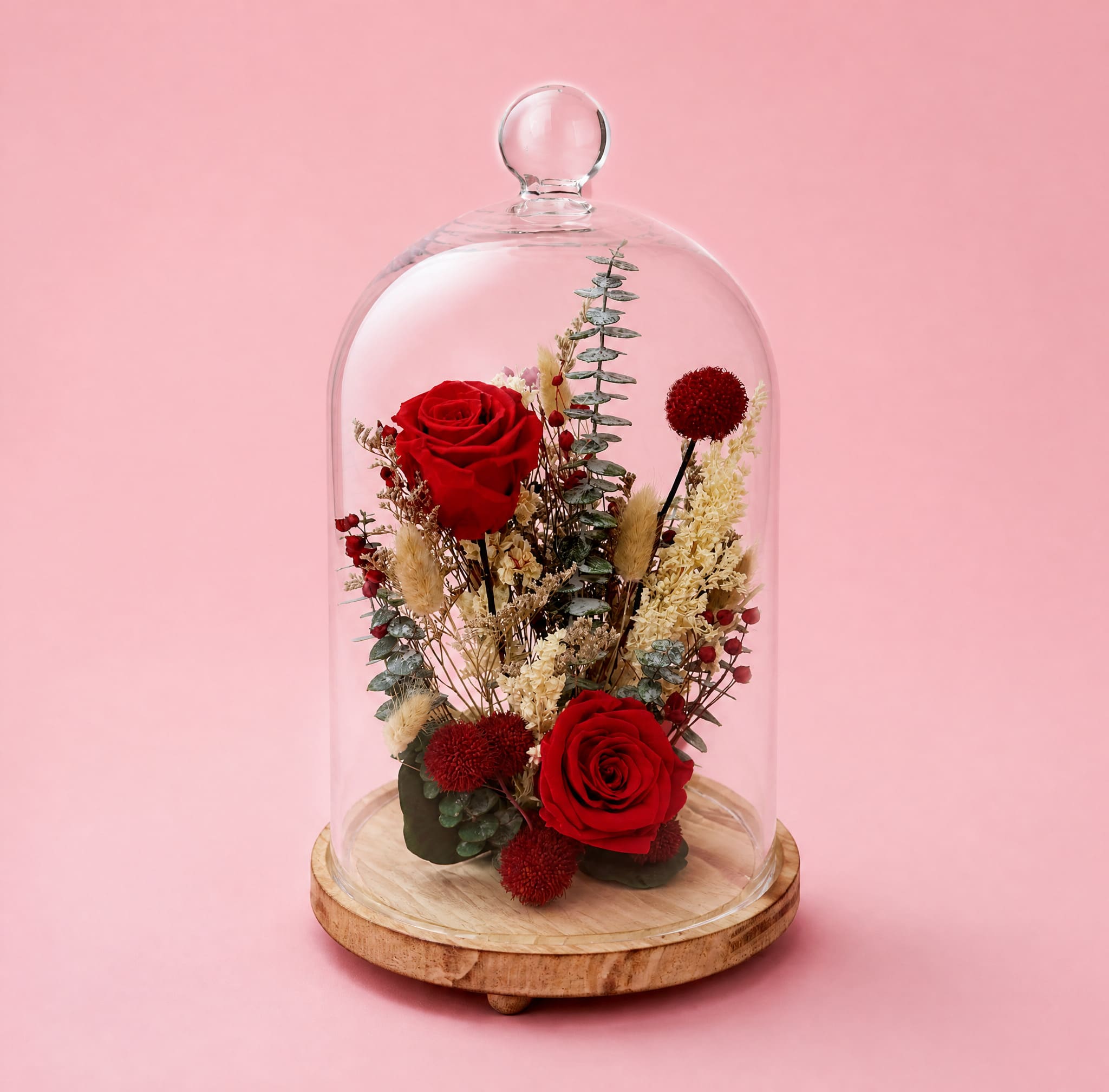 Red roses and dried flowers under a glass dome on a wooden base