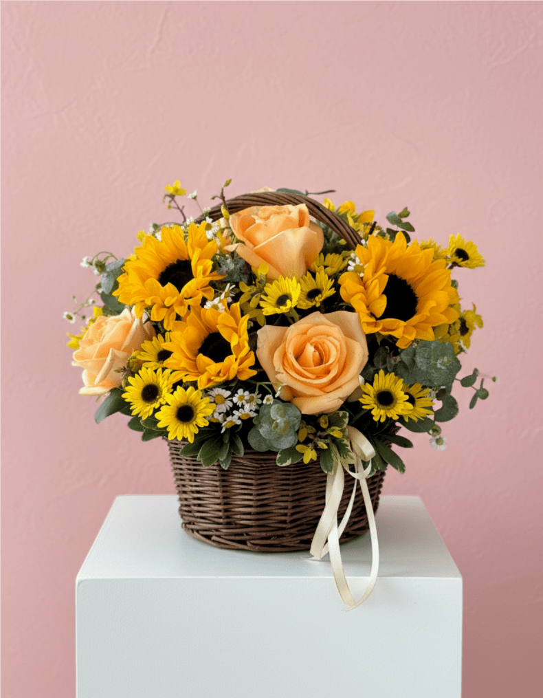 Basket arrangement of yellow sunflowers, peach roses, and small yellow daisies with a ribbon bow.