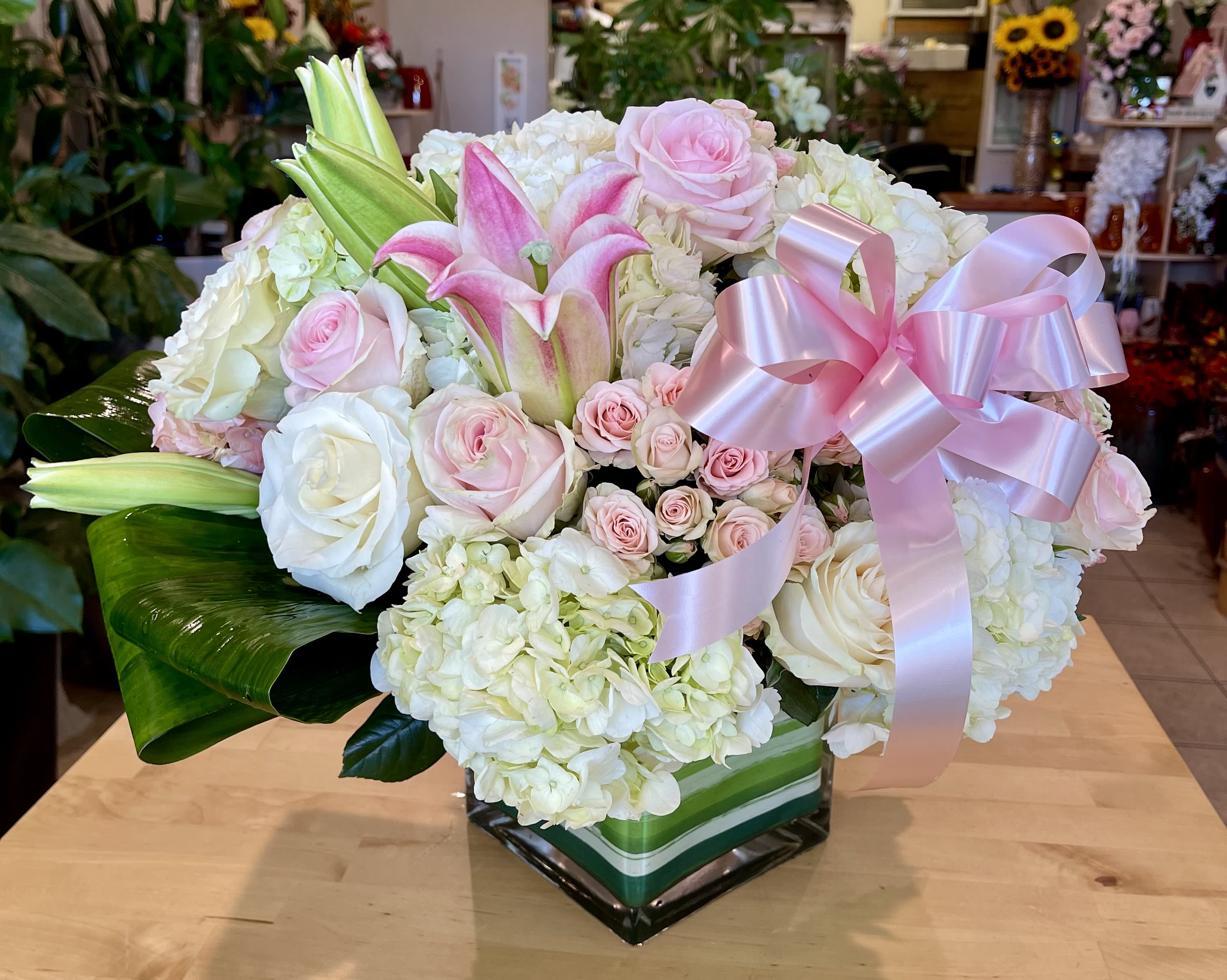 Pink and white floral arrangement with lilies, roses, and hydrangeas in a square vase