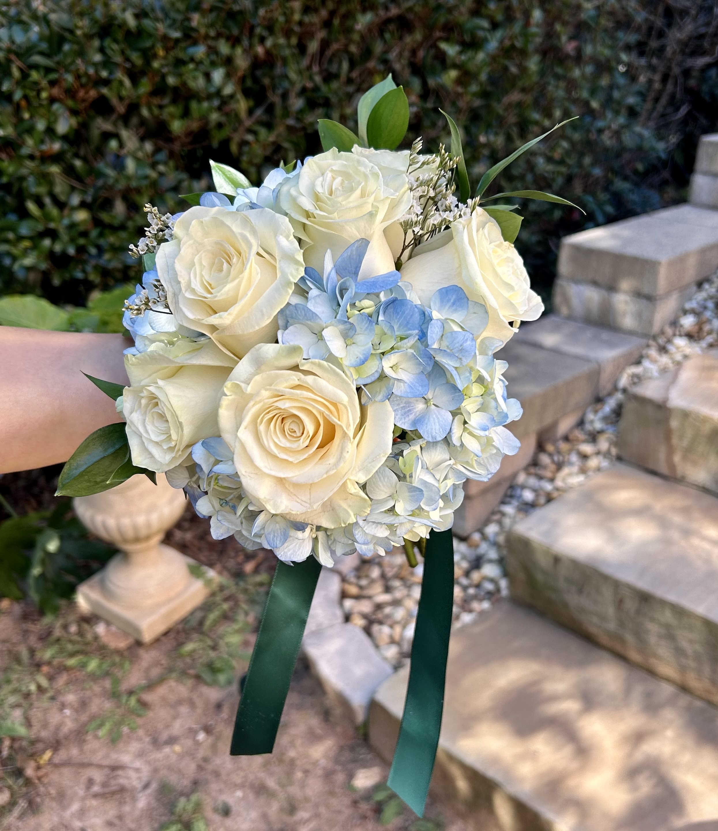 Handheld bouquet of white roses and pale blue hydrangeas with green ribbon
