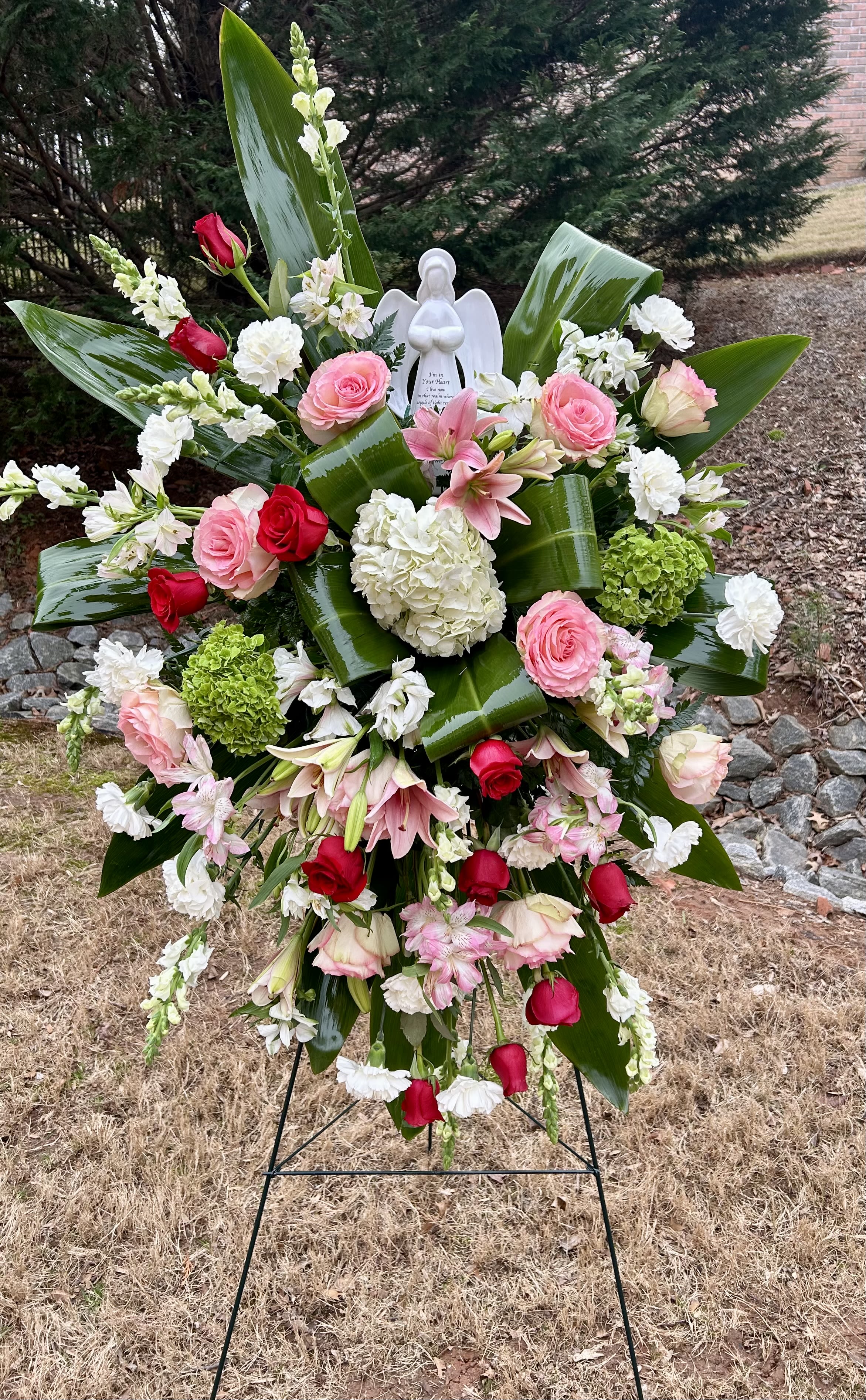 Standing floral spray with pink and red roses, white blooms, and an angel figurine