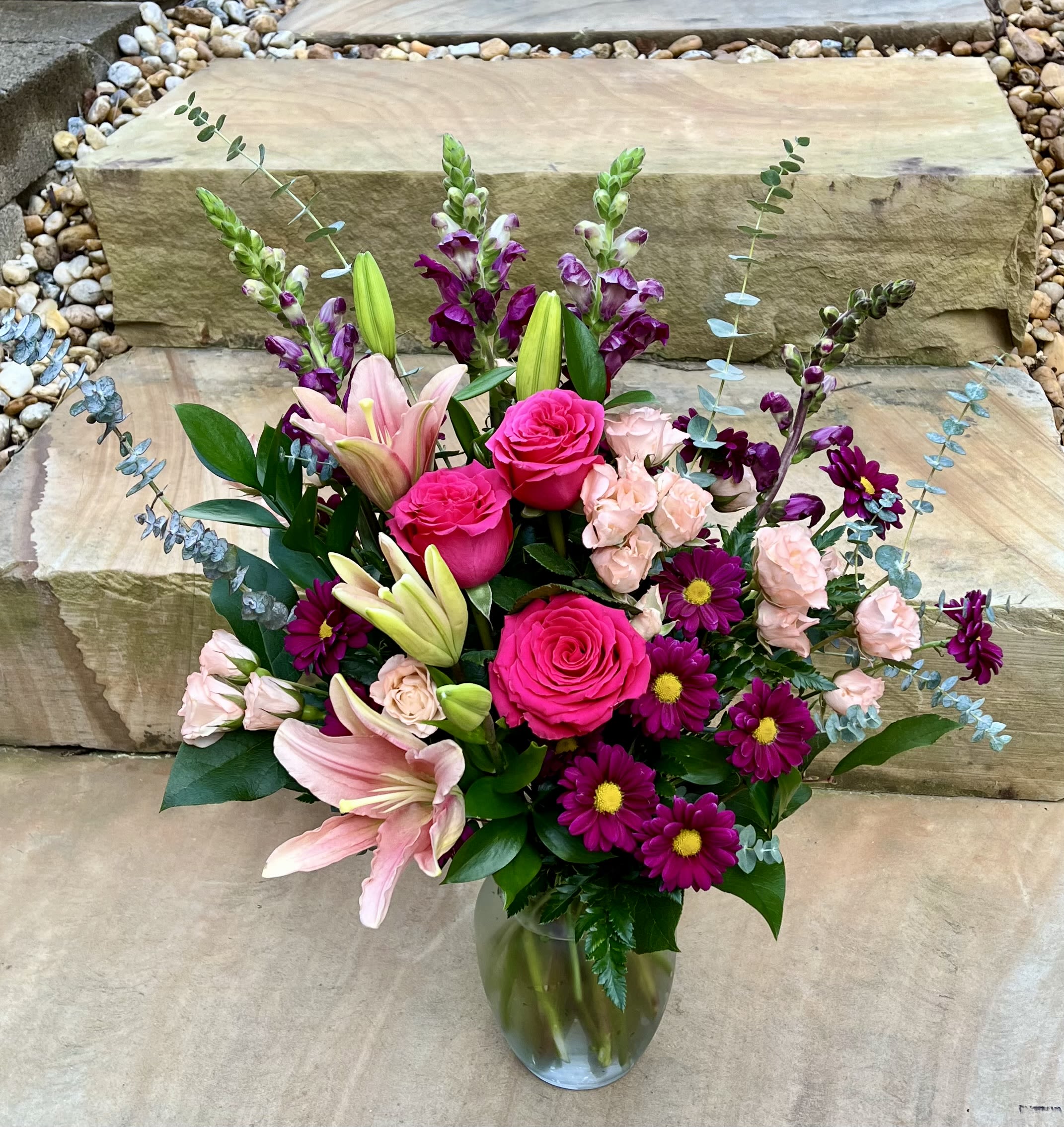 Bouquet of pink roses, lilies, and purple daisies in a glass vase
