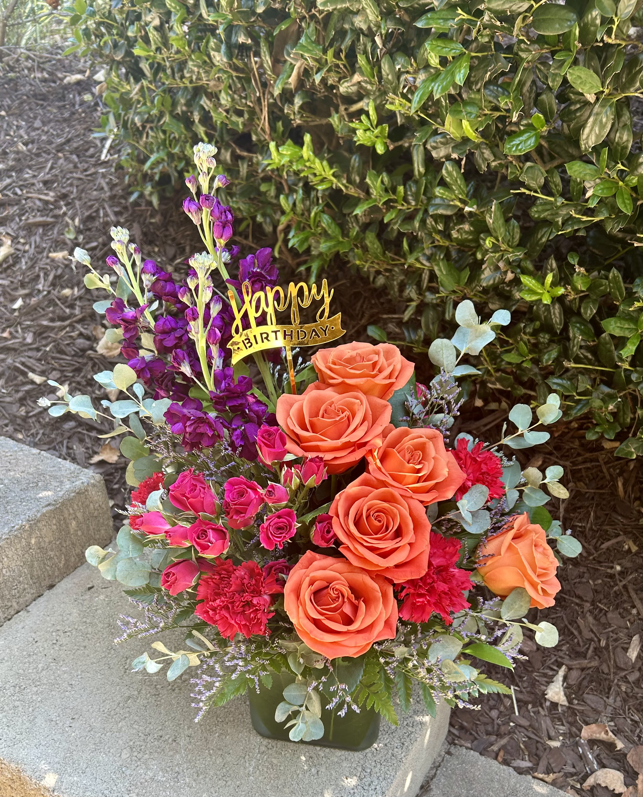 Orange and pink rose arrangement with a Happy Birthday pick in a vase