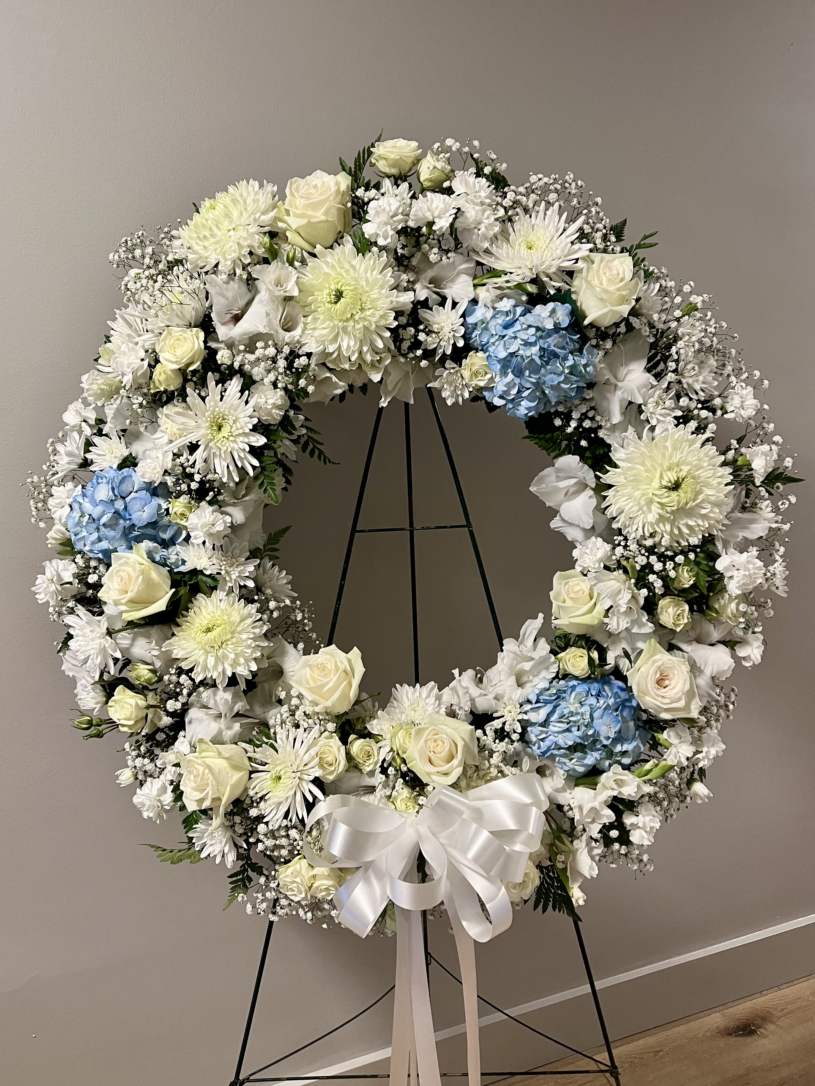 Large white floral wreath with blue hydrangeas on a black stand