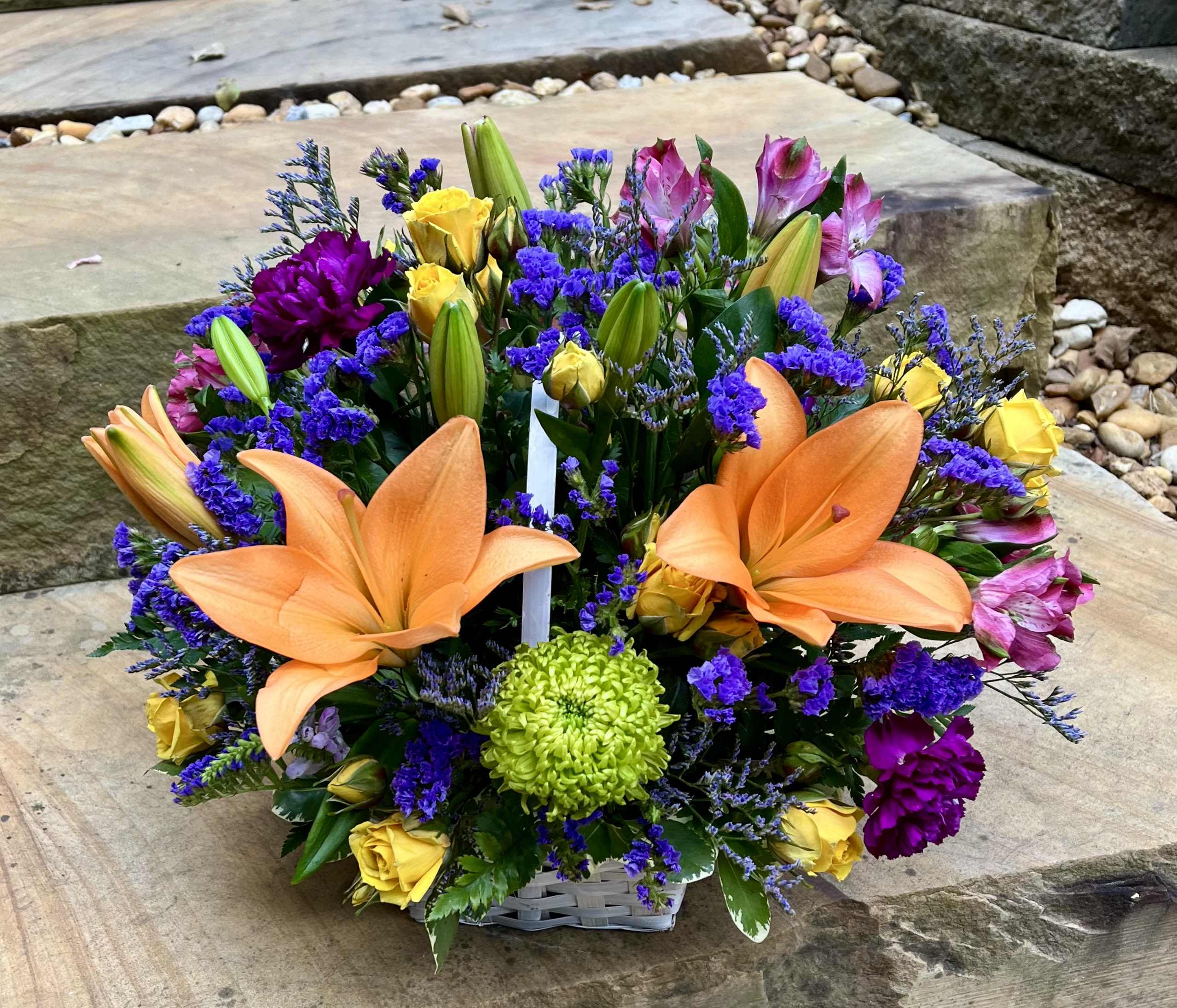 Mixed bouquet with orange lilies, yellow roses, and purple flowers in a basket