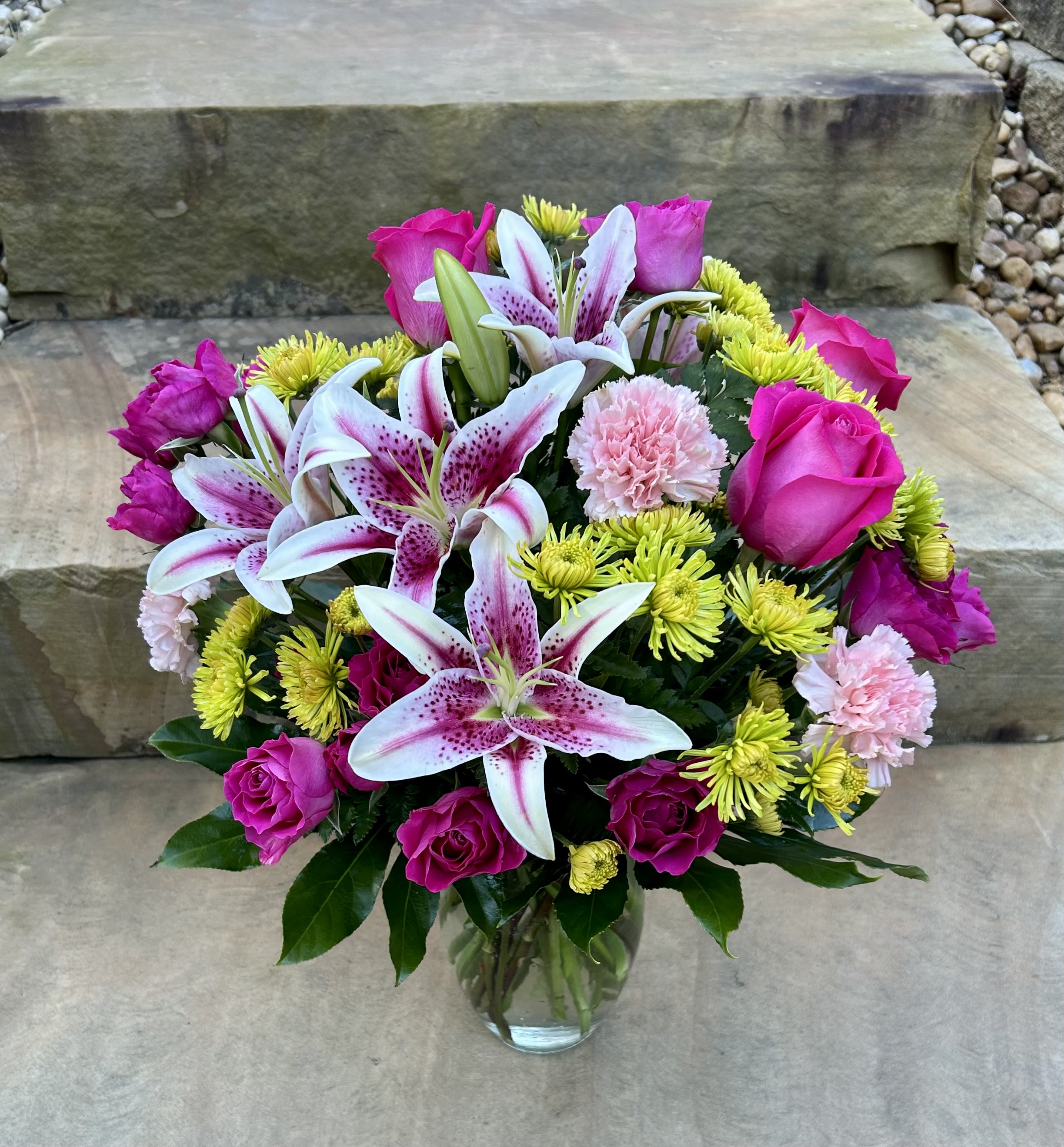 Bouquet of pink roses, lilies, and yellow mums in a glass vase
