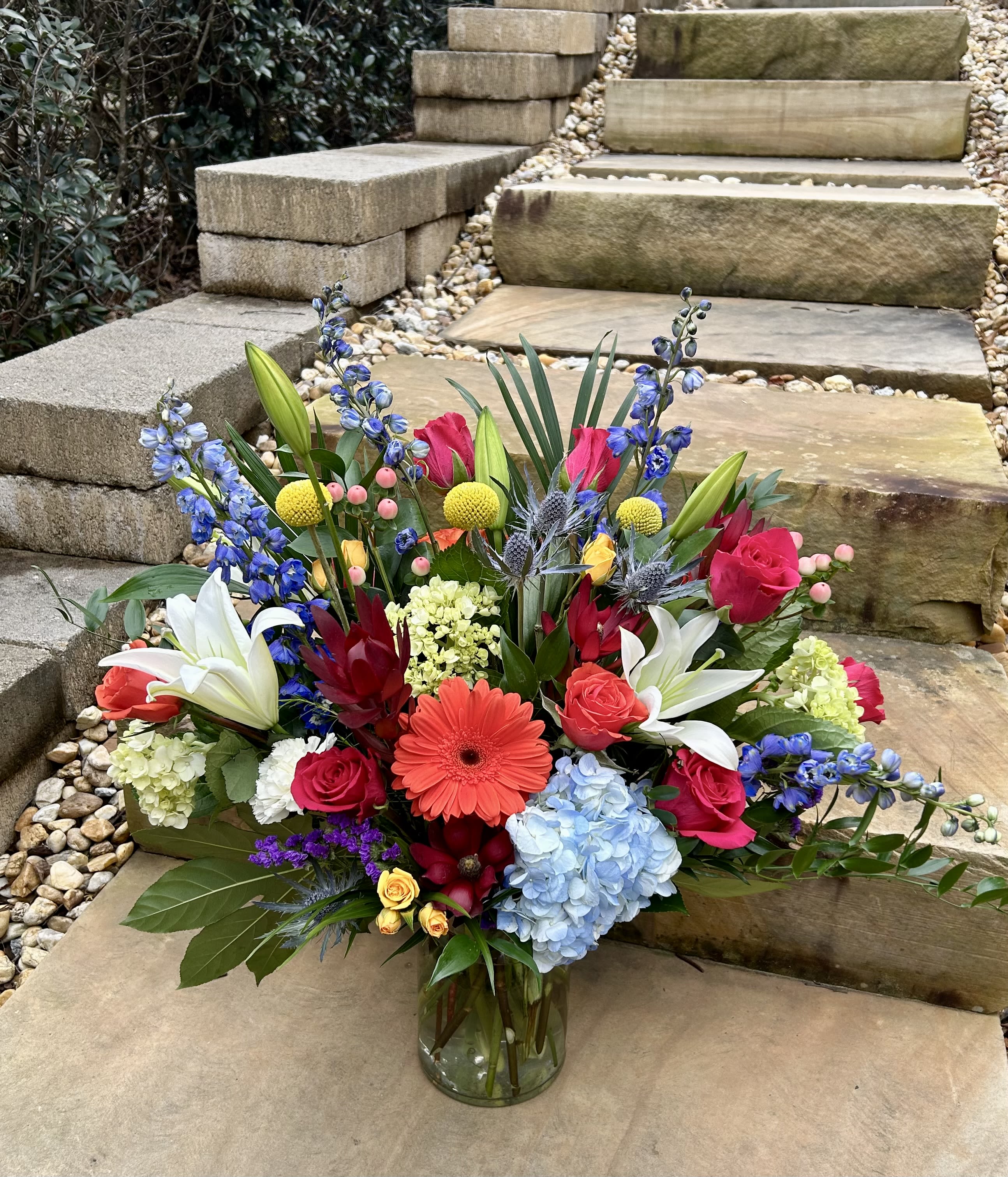 Colorful mixed bouquet in a glass vase with lilies, roses, hydrangea, and blue delphinium