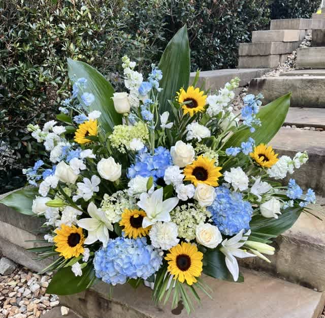 Large floral arrangement with sunflowers, white roses, blue hydrangeas, and white lilies