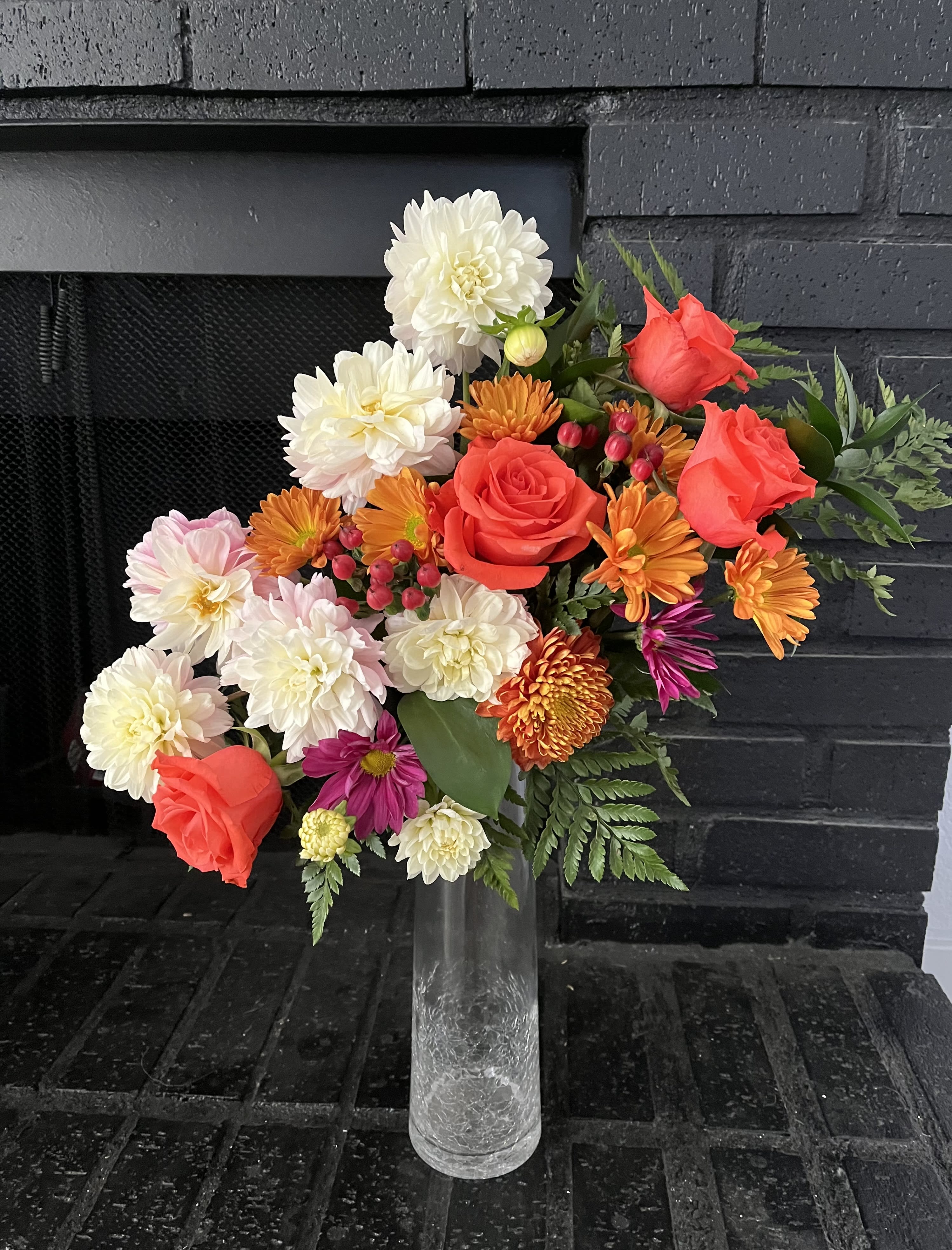 Mixed bouquet of red roses, white dahlias, and orange blooms in a clear vase