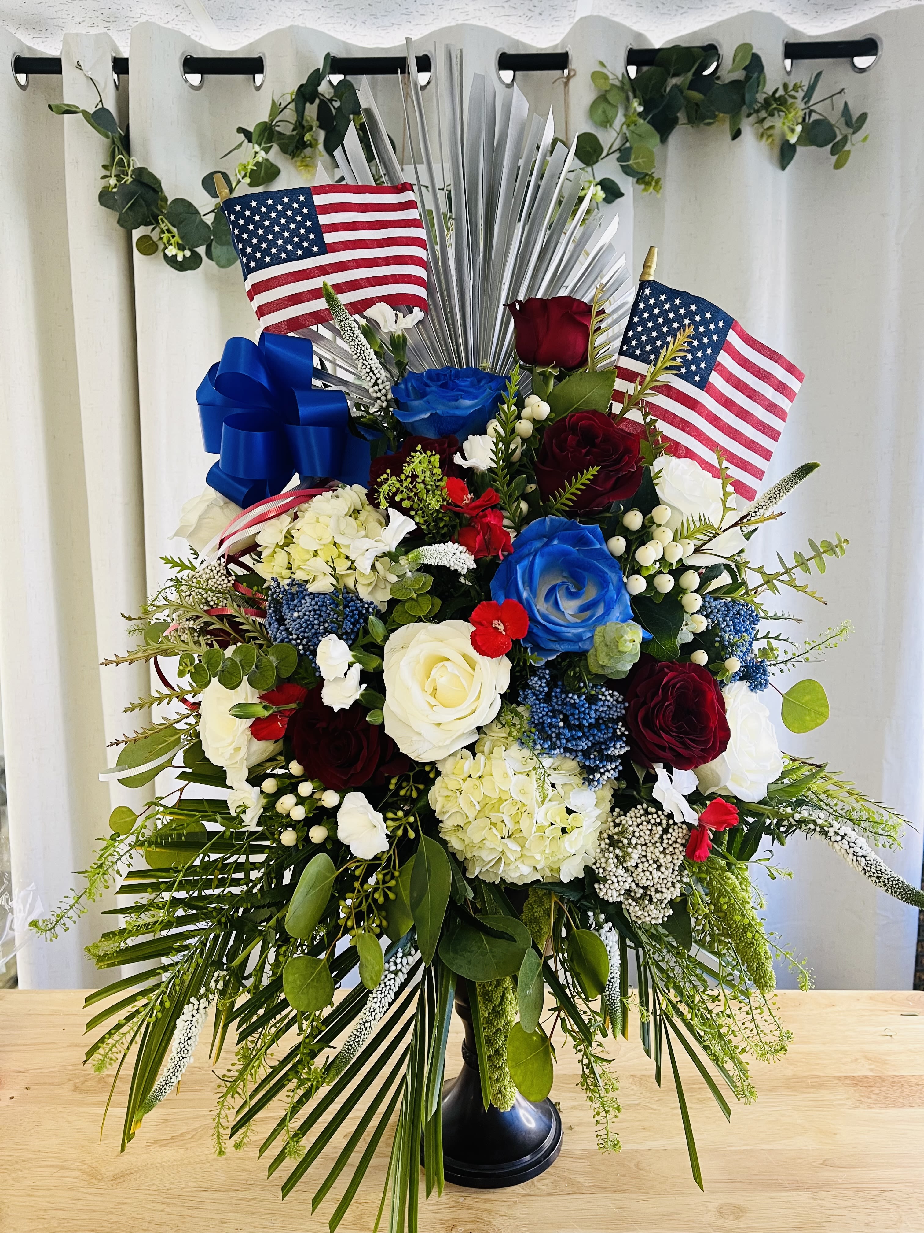 Large patriotic floral arrangement with red, white, and blue roses and flags