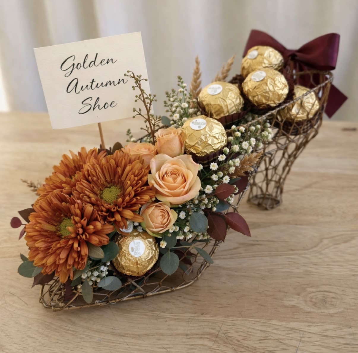 Orange flowers and gold chocolates arranged in a shoe-shaped basket