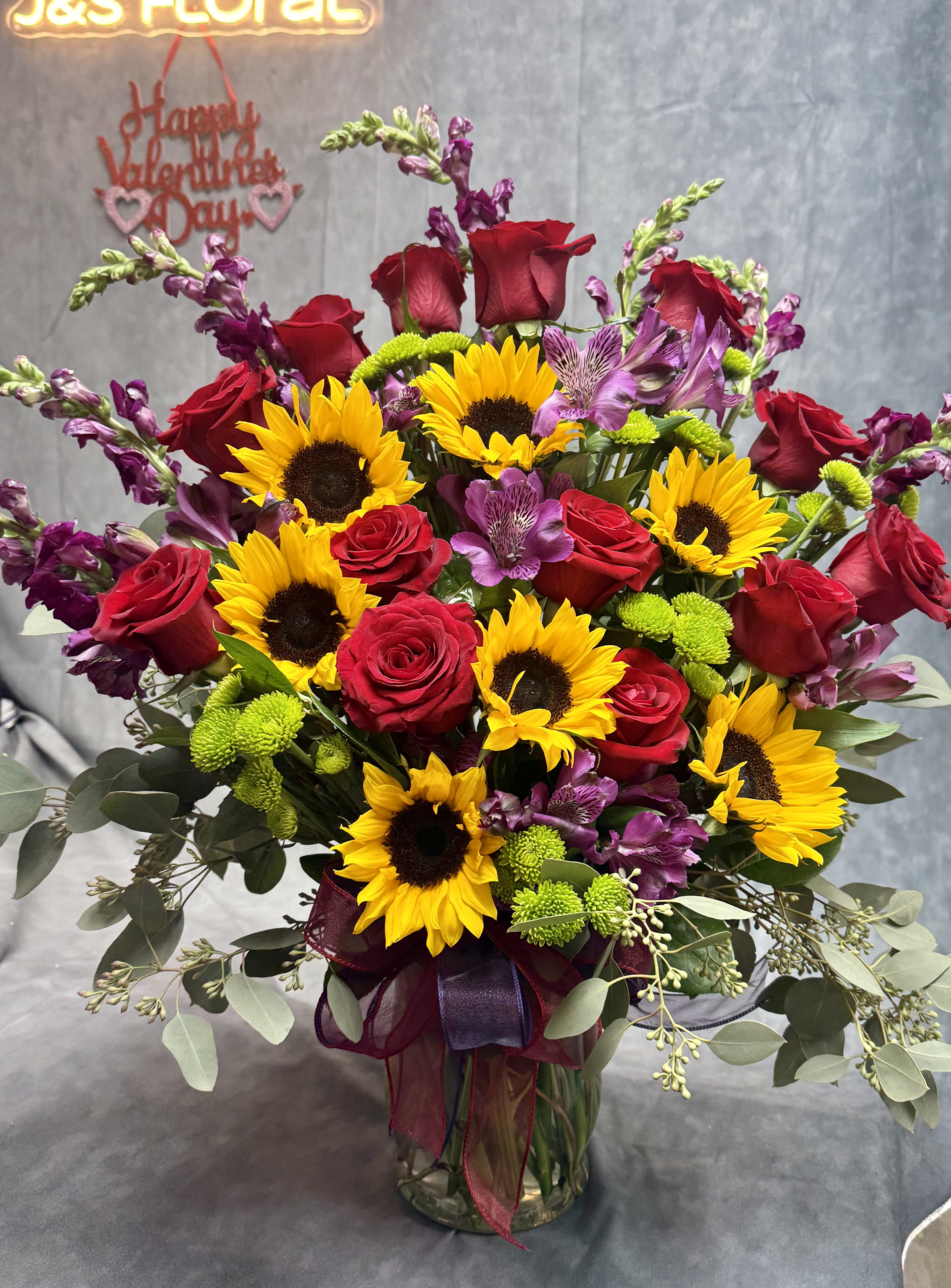 Bouquet of red roses, sunflowers, and purple flowers in a glass vase